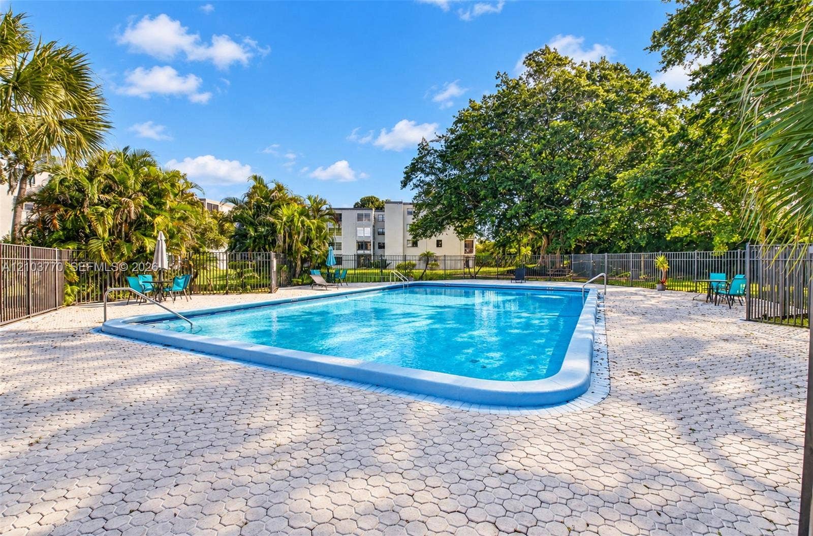 9440 SW 8th Street, #309, Boca Raton, Boca Raton, FL 33428 Rectangular swimming pool with a blue tiled border, surrounded by interlocking paver decking and a black metal fence