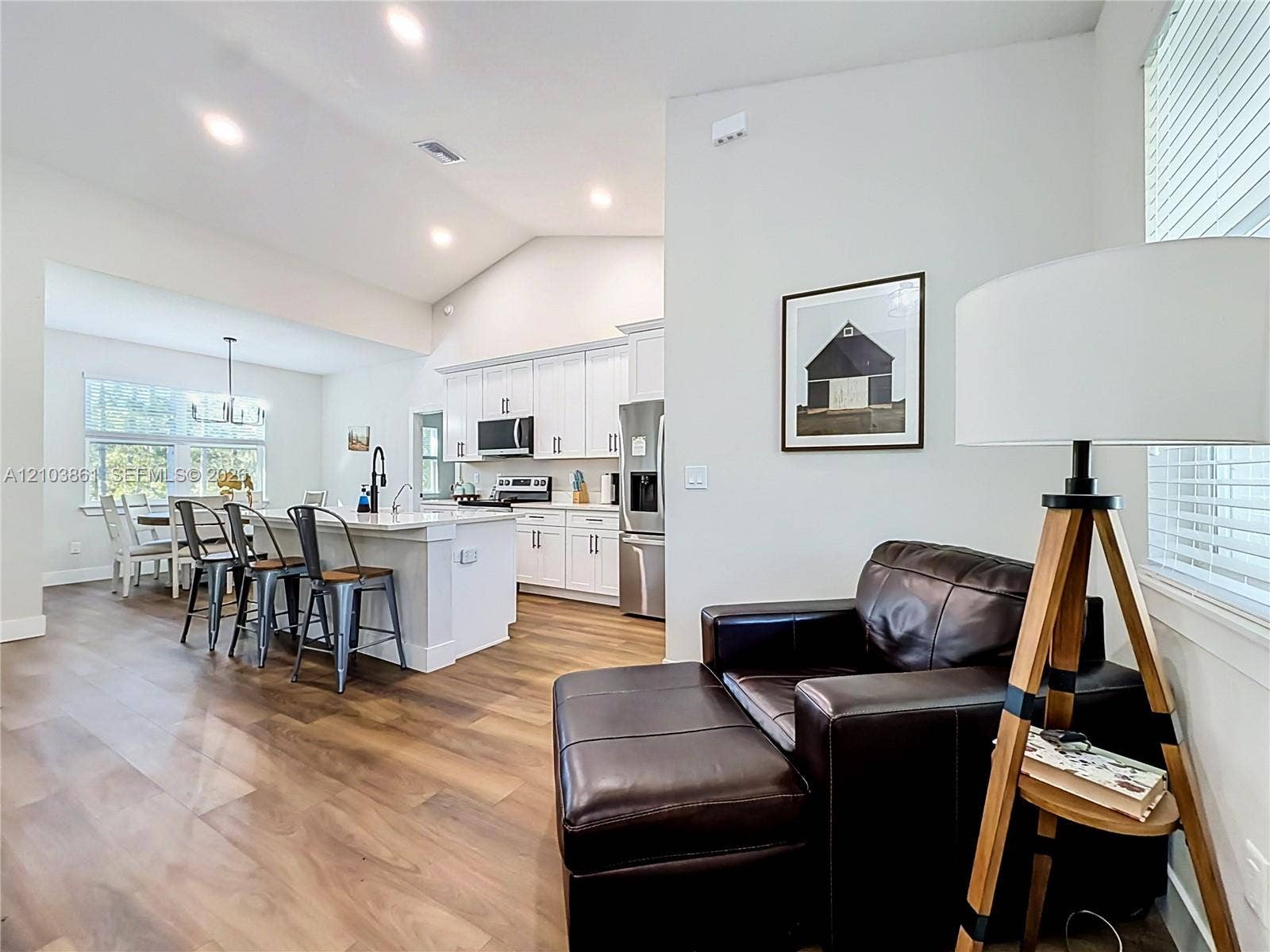 Vaulted ceilings, wood-finish flooring, white shaker-style cabinetry, kitchen island with stone-finish countertop, and recessed lighting