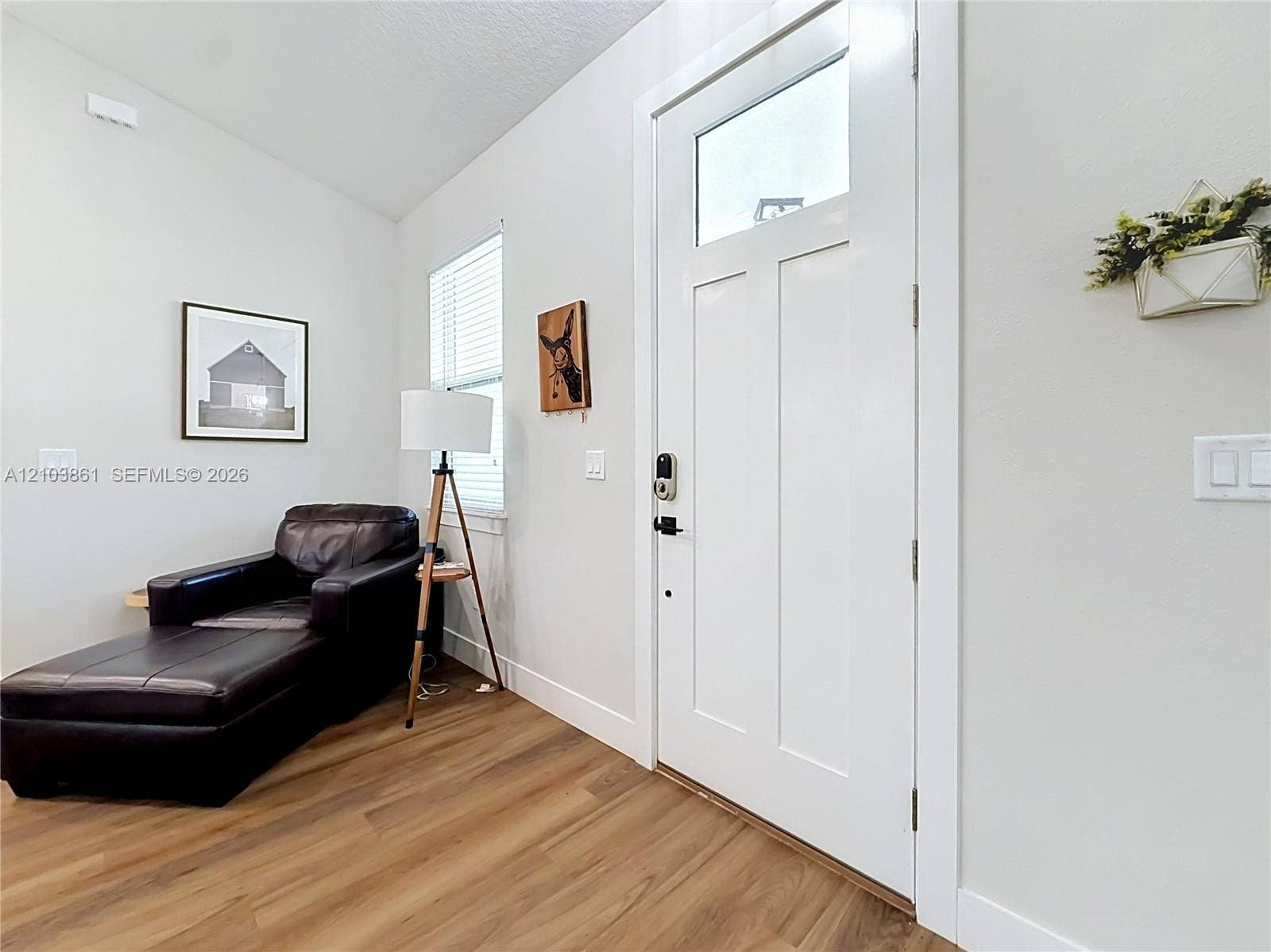 Entrance featuring a white door with an upper glass pane, neutral wall paint, wood-finish flooring, and a single-hung window with blinds