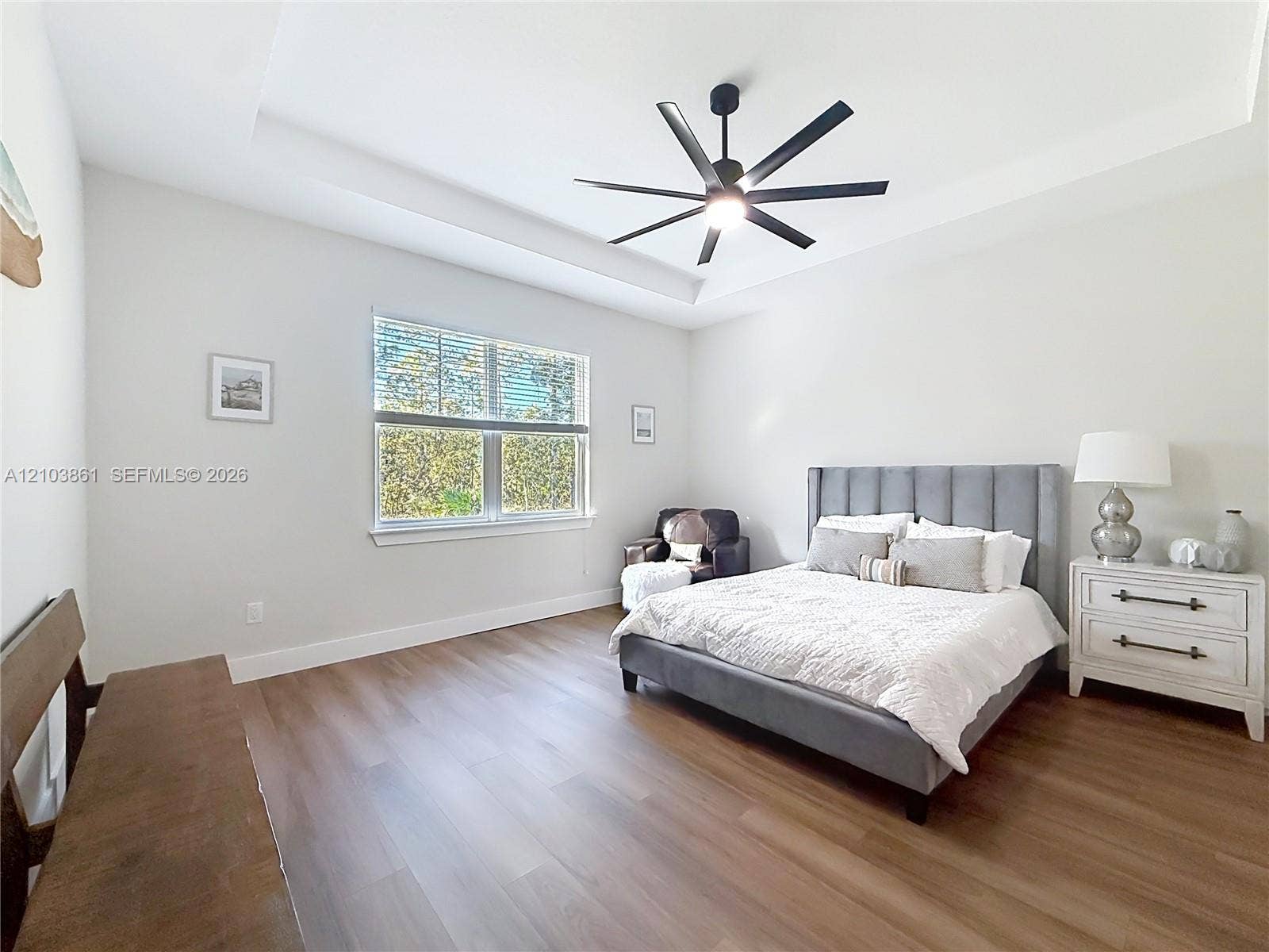 Tray ceiling with integrated lighting, wood-finish flooring, and a multi-blade ceiling fan