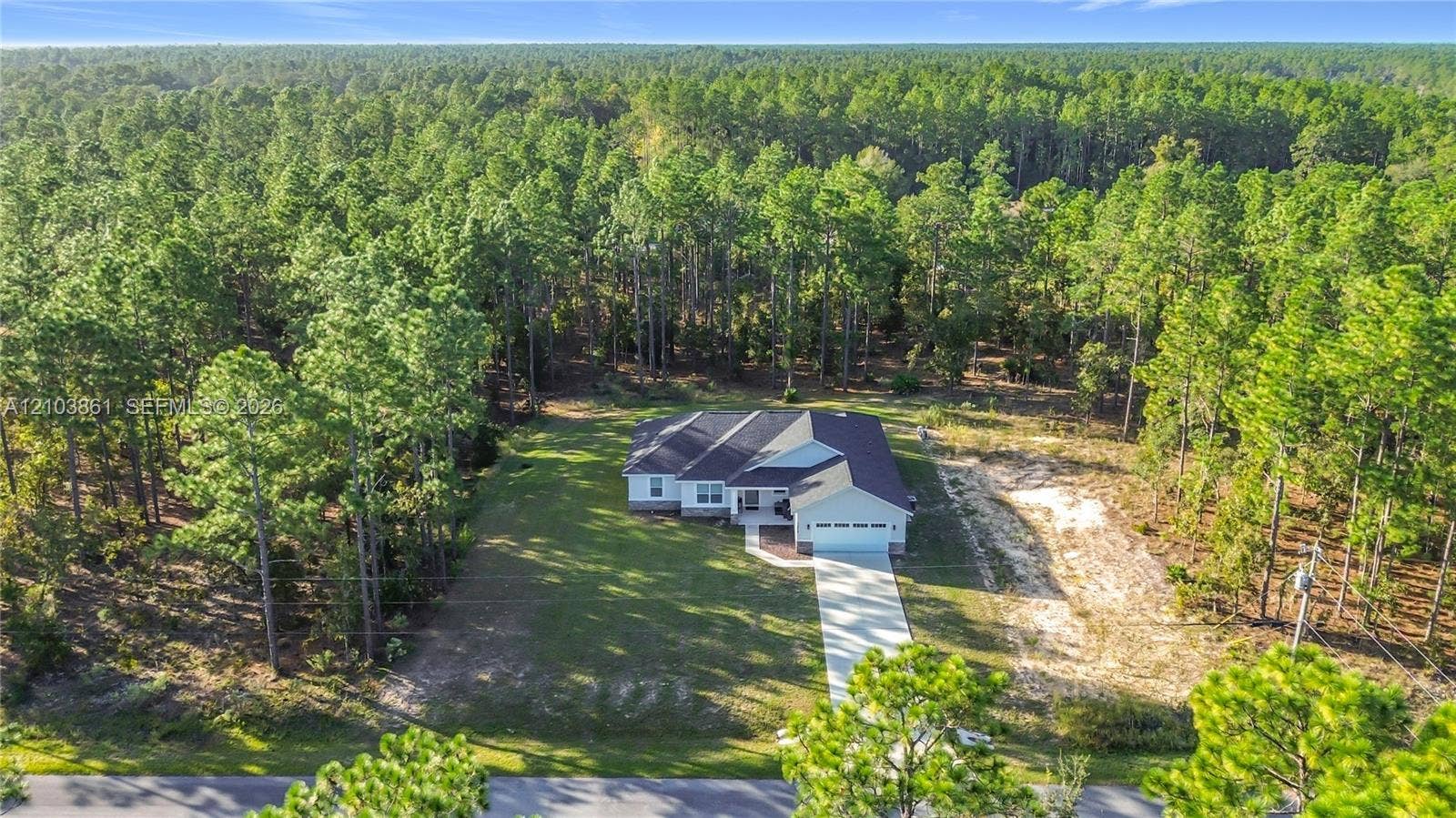 Single-story residence with a multi-gable roofline, concrete driveway, attached garage, and surrounding mature pine forest