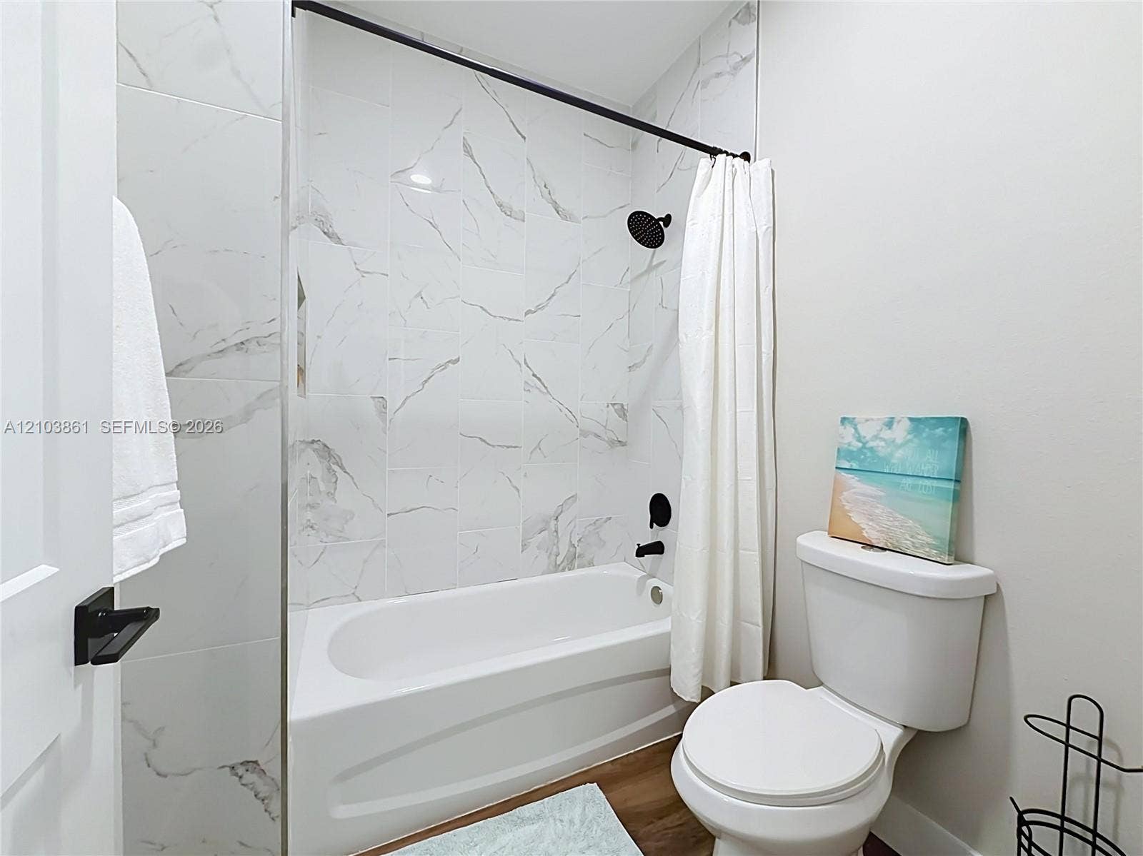 Bathroom featuring a tub-shower combination with floor-to-ceiling large-format veined tile surround, matte black rainfall showerhead, matching matte black plumbing fixtures, and wood-finish flooring