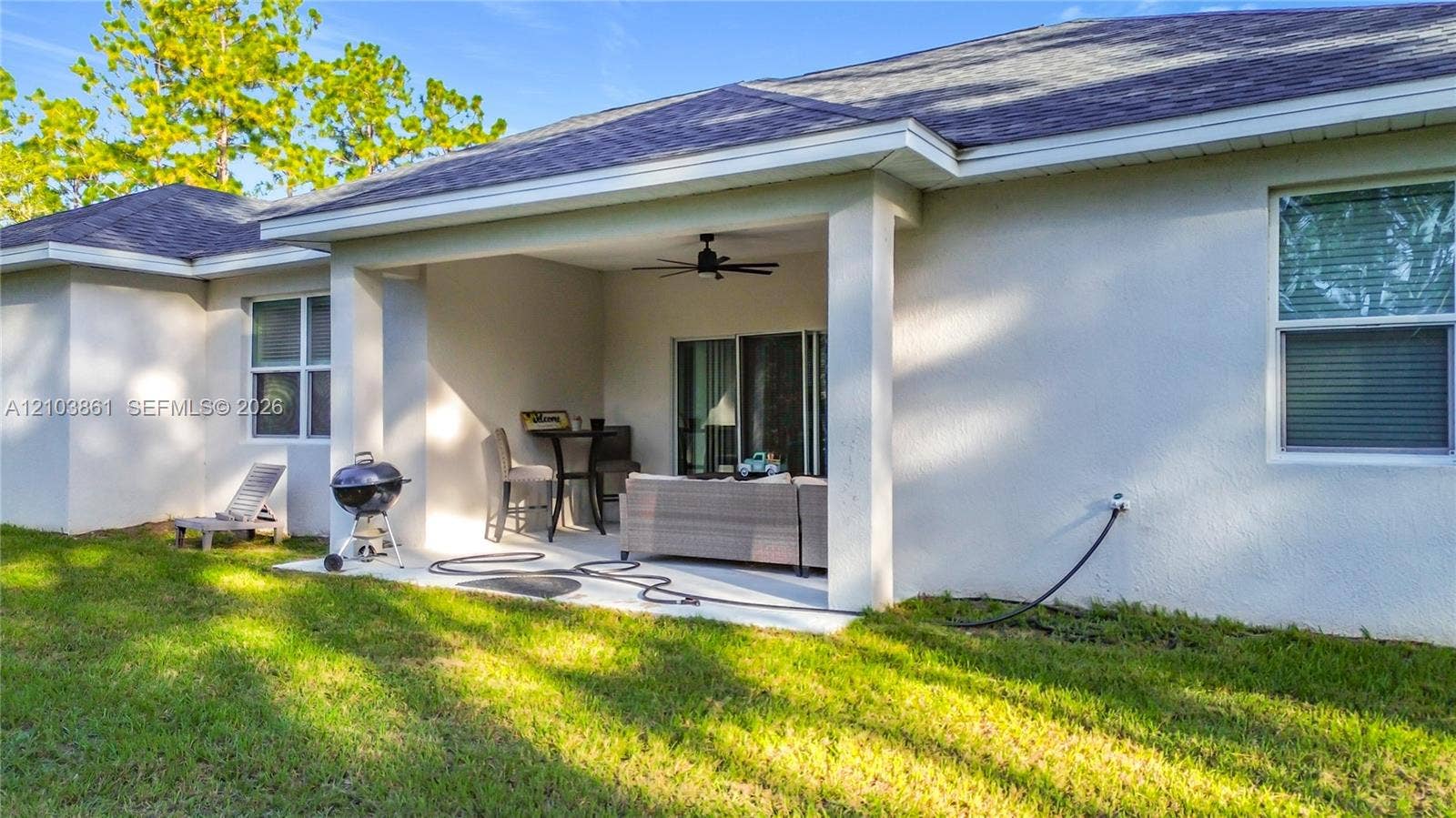 Covered concrete patio featuring a ceiling fan, light-colored stucco exterior, sliding glass doors, and grass yard
