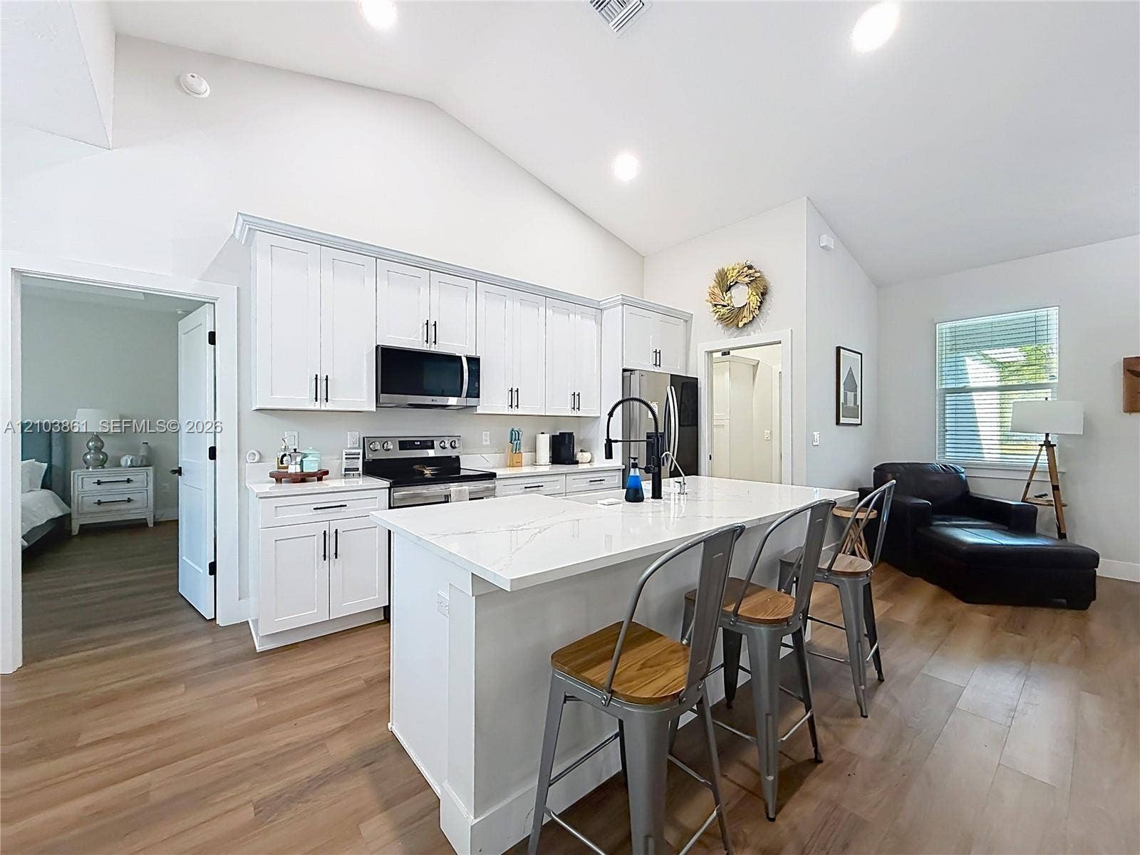 Kitchen featuring white cabinetry, quartz countertops, a central island, stainless steel appliances, and wood-finish flooring under vaulted ceilings