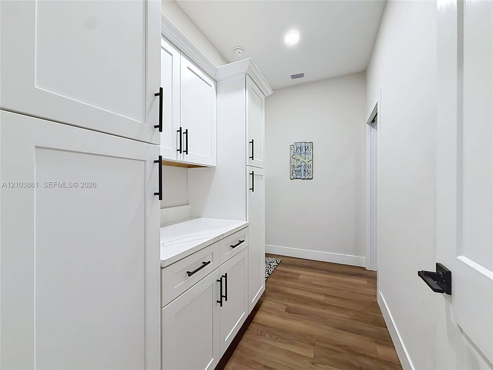 White shaker-style cabinetry with matte black hardware, stone-finish countertops, wood-finish flooring, and recessed ceiling lighting