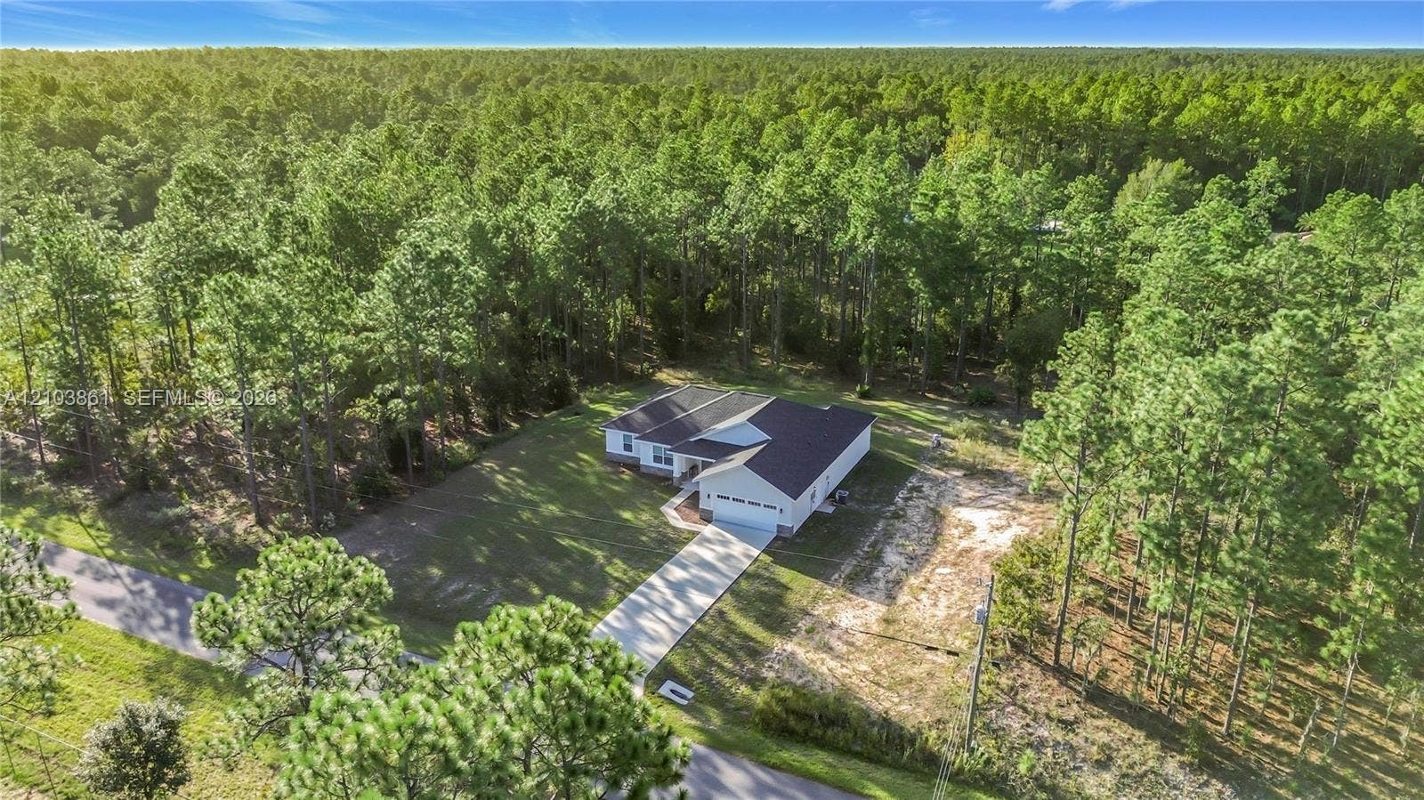 Single-story residence featuring a multi-gabled roofline, concrete driveway, two-car garage, and a lot bordered by mature coniferous woodland