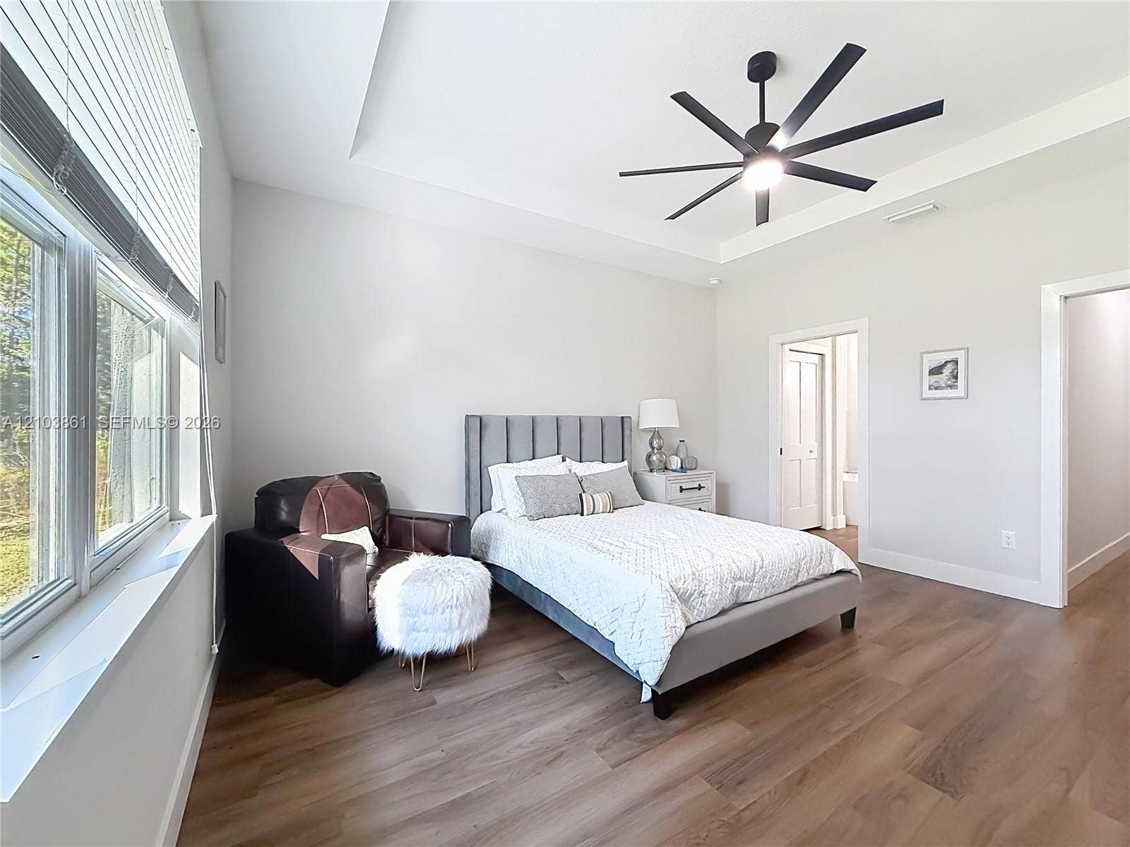 Bedroom featuring a tray ceiling, multi-blade ceiling fan, wood-finish flooring, and large windows with blinds