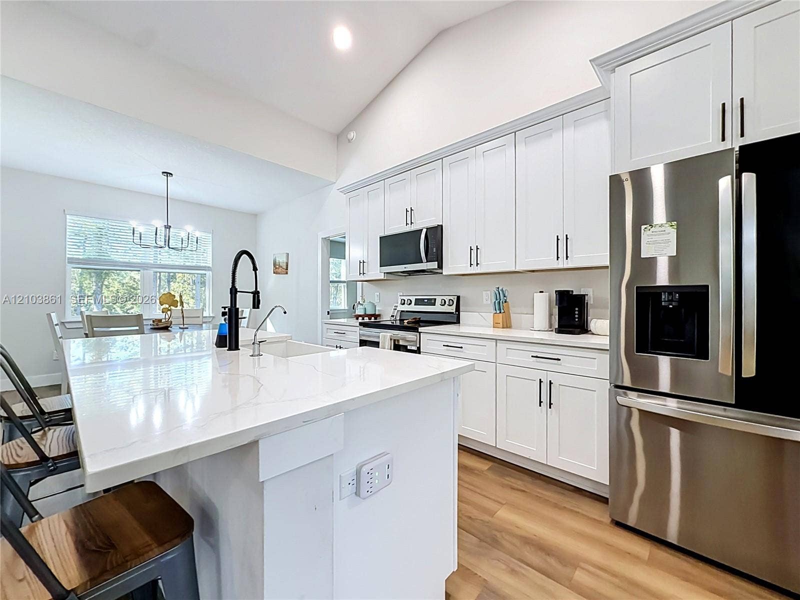 Kitchen featuring white Shaker-style cabinetry, a central island with a solid-surface countertop, stainless steel appliances, a matte black high-arc faucet, and wood-finish flooring
