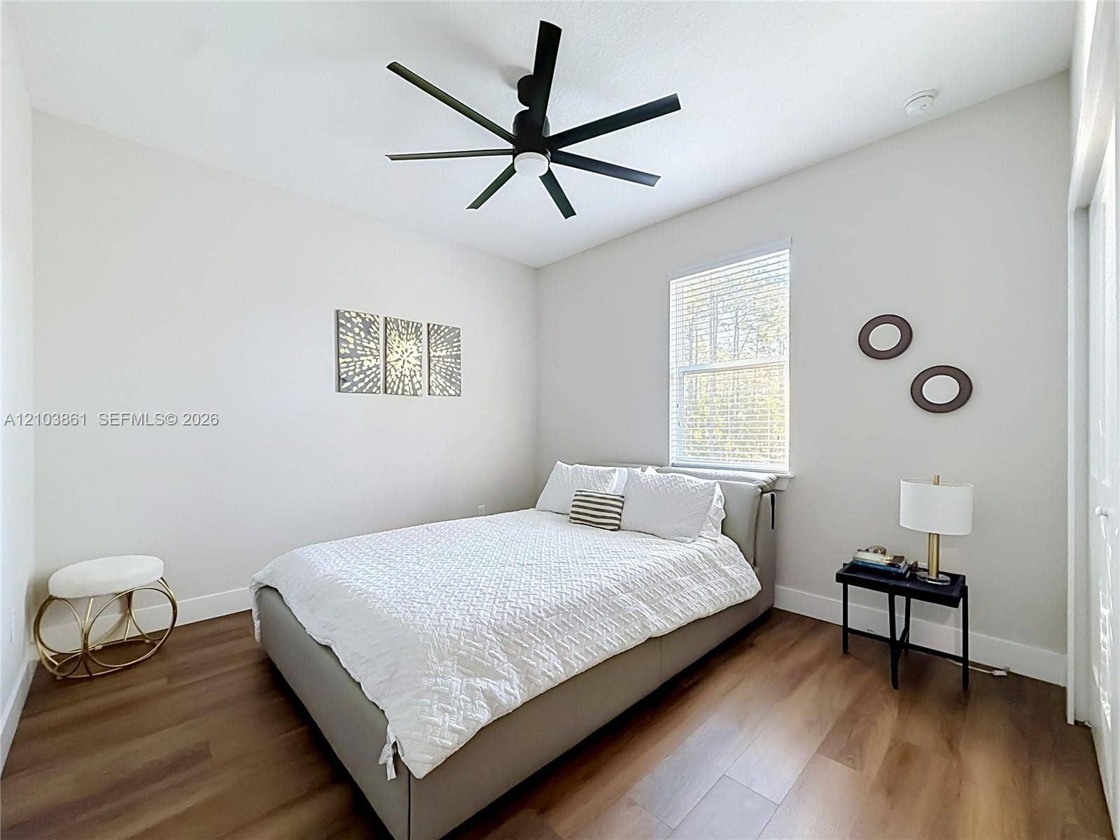 Wood-finish flooring, multi-blade matte black ceiling fan, and window with integrated blinds