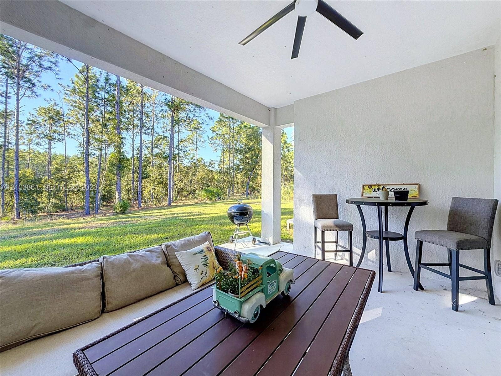 Covered patio featuring a painted concrete floor, ceiling-mounted fan, and exterior-facing structural pillars overlooking a lawn with mature trees