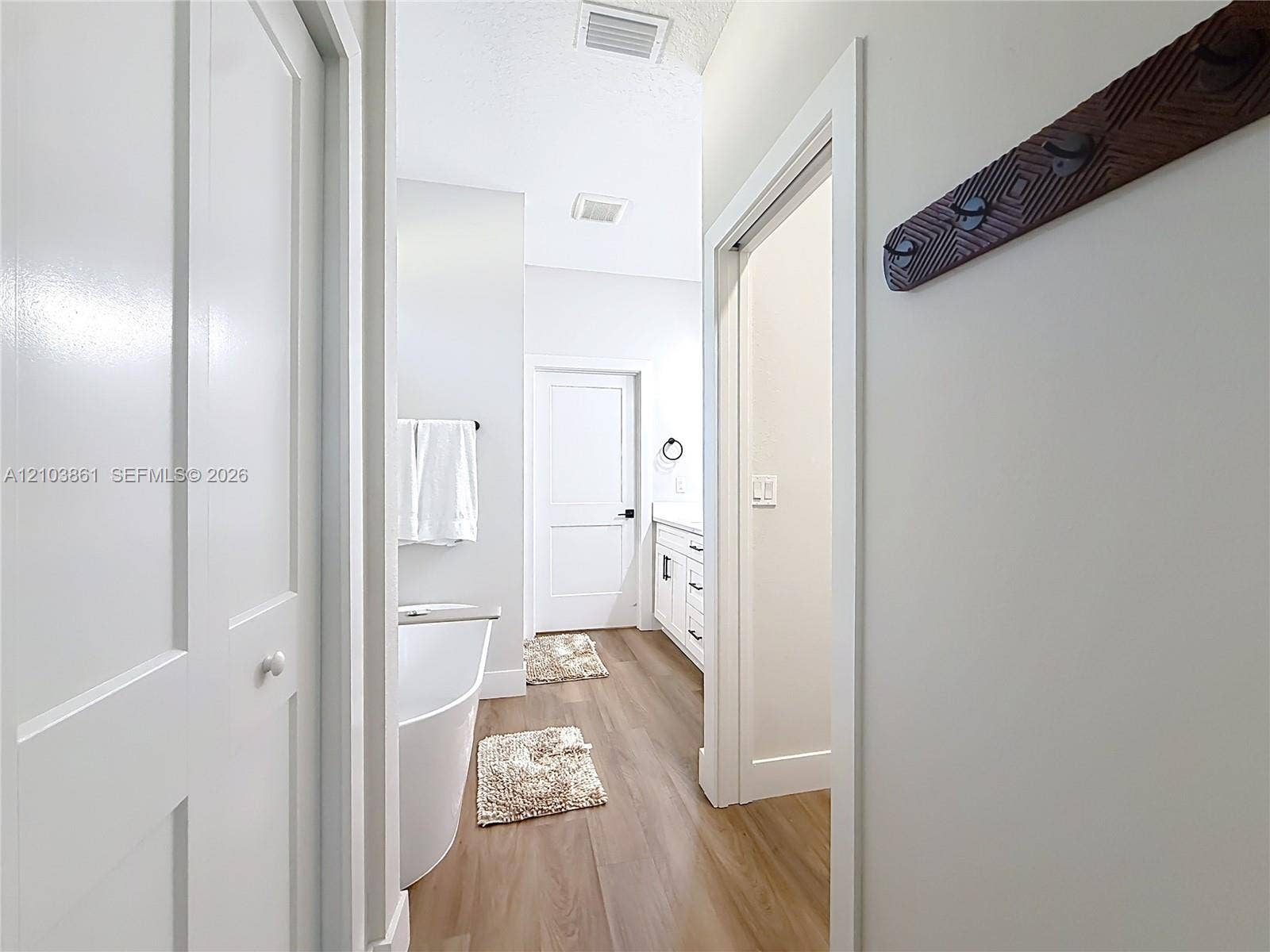Bathroom featuring a freestanding soaking tub, white shaker-style cabinetry with neutral countertops, wood-finish flooring, and multi-panel interior doors
