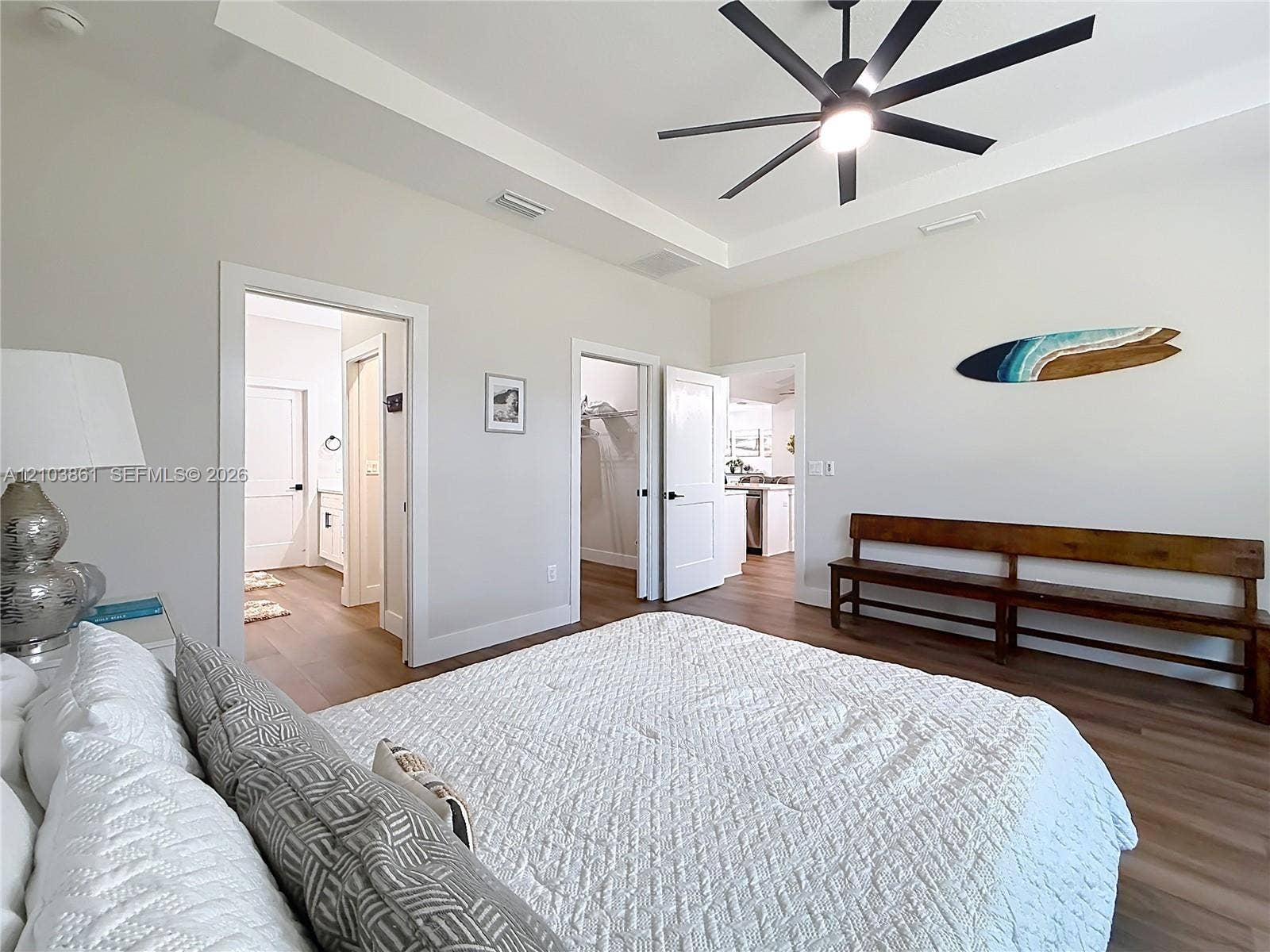 Tray ceiling featuring a multi-blade matte black ceiling fan, complemented by wood-finish flooring and solid-core interior doors