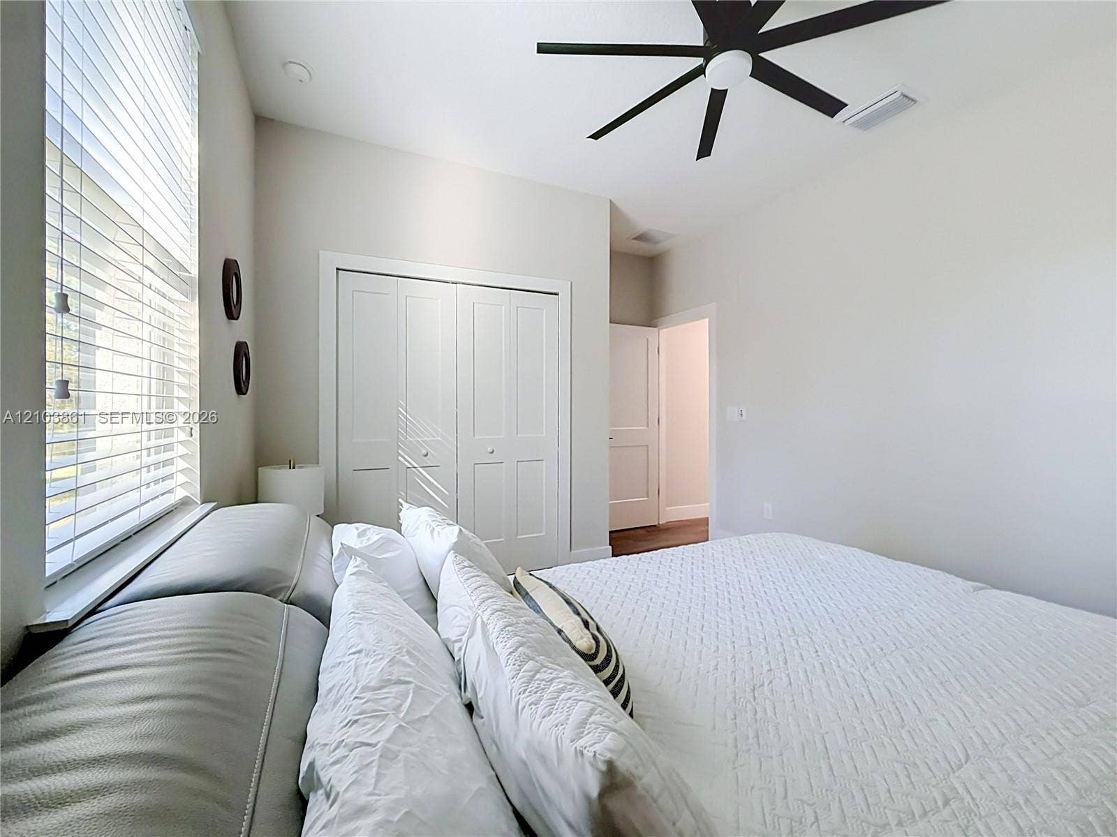 Neutral interior featuring high ceilings, a multi-blade matte black ceiling fan, white paneled closet doors, and horizontal slat window blinds
