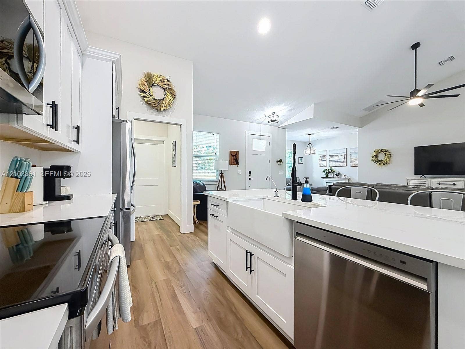 Kitchen featuring white cabinetry, quartz countertops, a farmhouse-style apron sink, matte black hardware, and wood-finish flooring