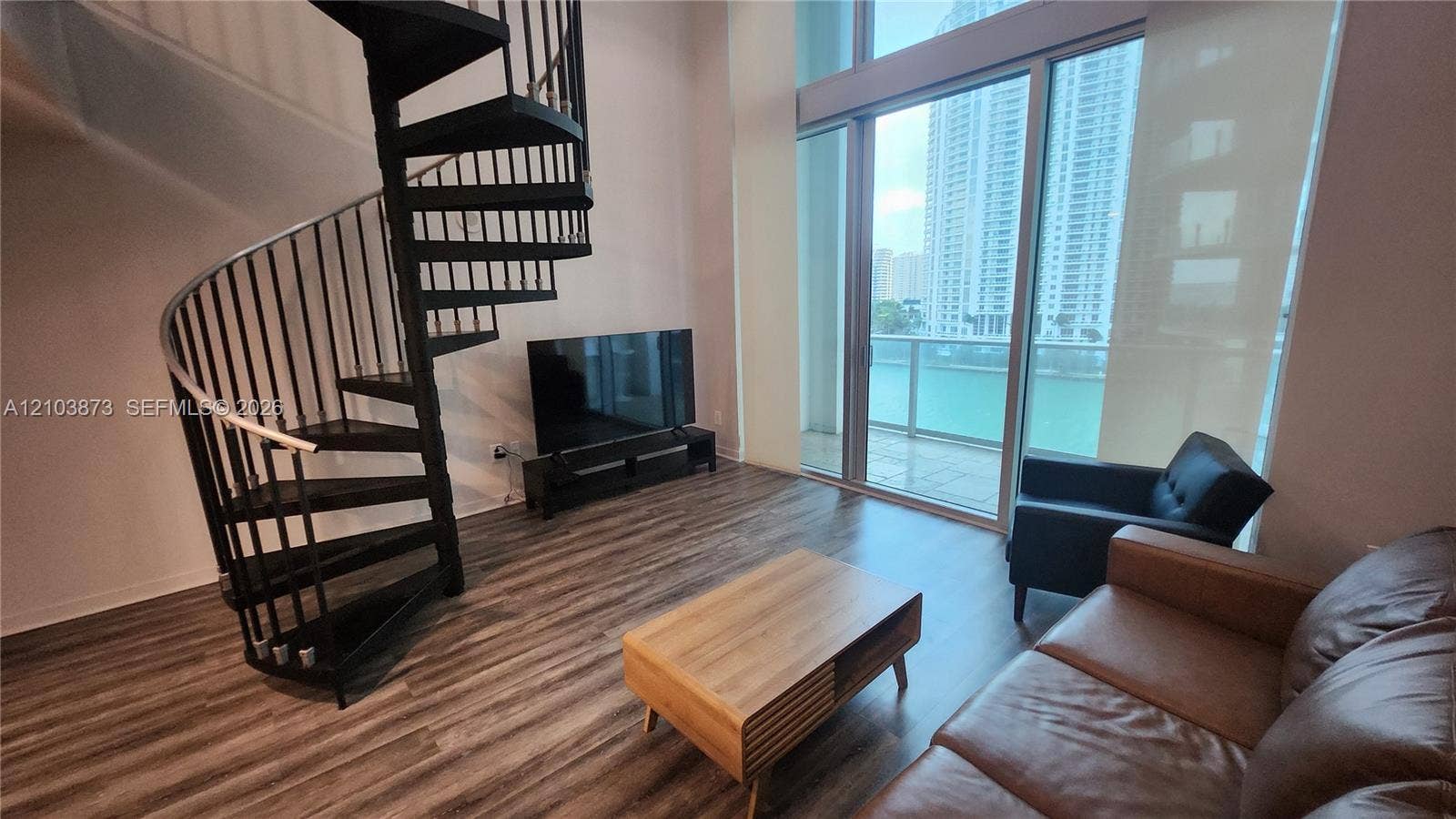 300 S Biscayne Boulevard, #L-808, Miami, FL 33131 Double-height ceilings featuring floor-to-ceiling windows, wood-finish flooring, and a black metal spiral staircase