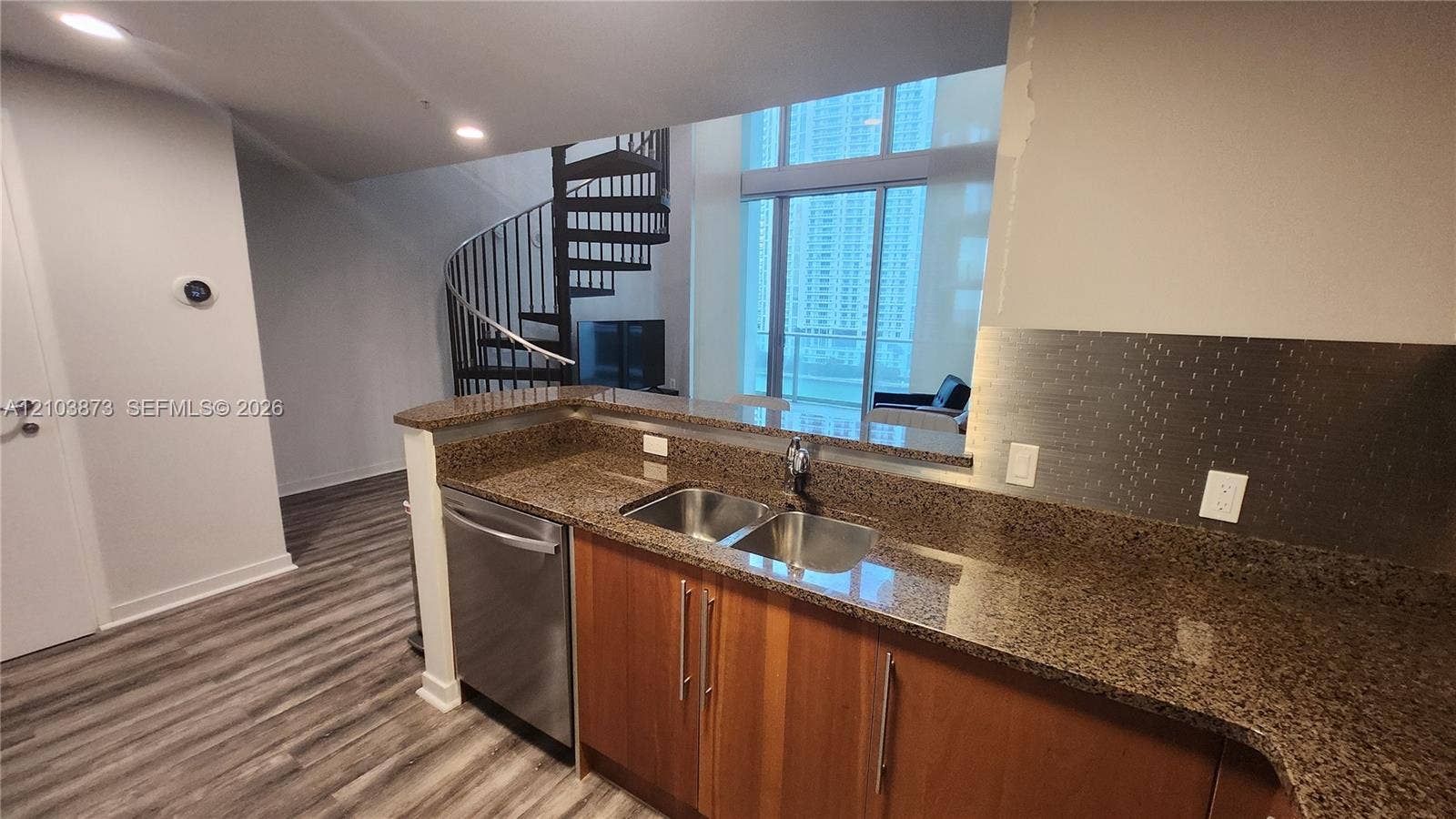 300 S Biscayne Boulevard, #L-808, Miami, FL 33131 Kitchen featuring stone countertops, stainless steel dual-basin sink, wood-finish cabinetry, and stainless steel dishwasher, complemented by a metal spiral staircase and floor-to-ceiling windows