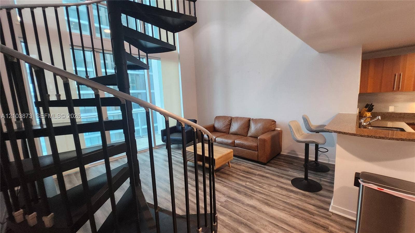 300 S Biscayne Boulevard, #L-808, Miami, FL 33131 Black metal spiral staircase with wood treads, soaring cathedral ceilings, expansive floor-to-ceiling windows, wood-finish flooring, and a kitchen breakfast bar with stone-surfaced countertop