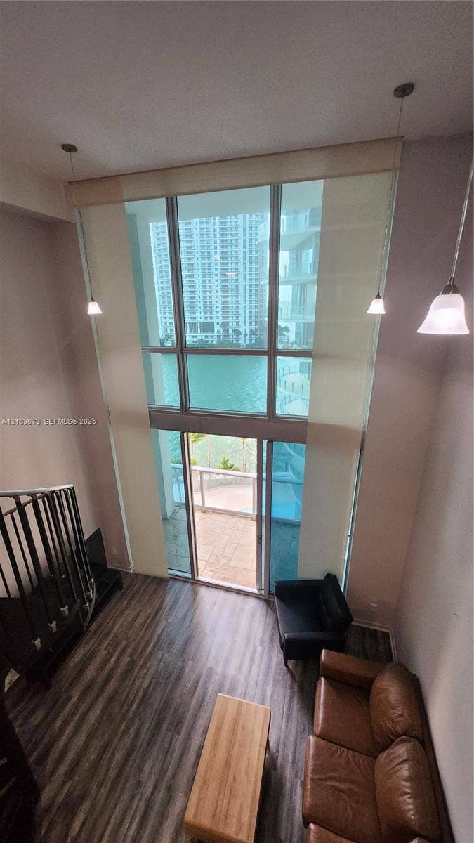 300 S Biscayne Boulevard, #L-808, Miami, FL 33131 Double-height floor-to-ceiling windows, wood-finish flooring, metal staircase railing, and multiple pendant light fixtures