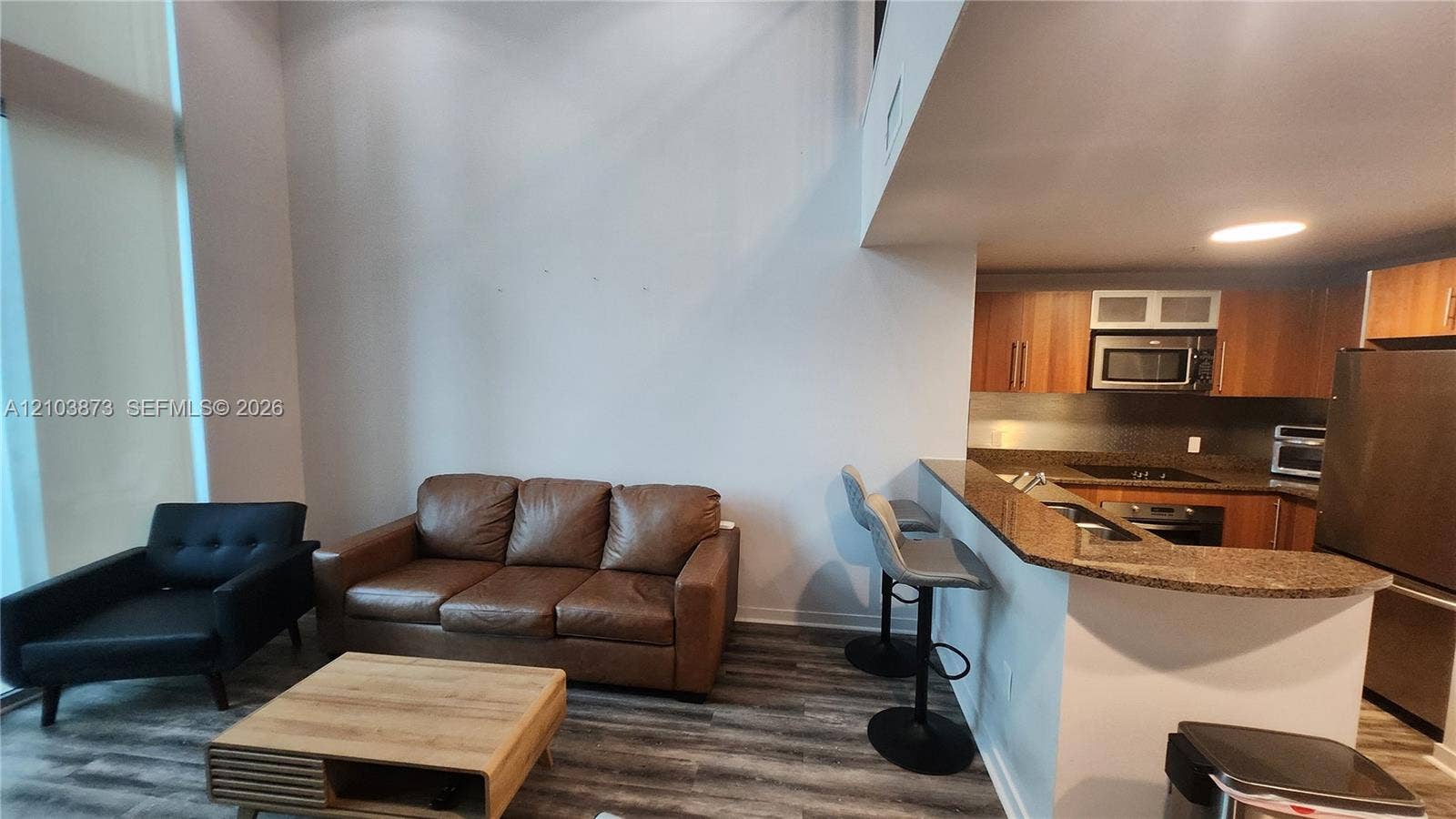 300 S Biscayne Boulevard, #L-808, Miami, FL 33131 Double-height ceiling, kitchen peninsula with stone-surface countertop, wood-finish flooring, and cabinetry with integrated microwave