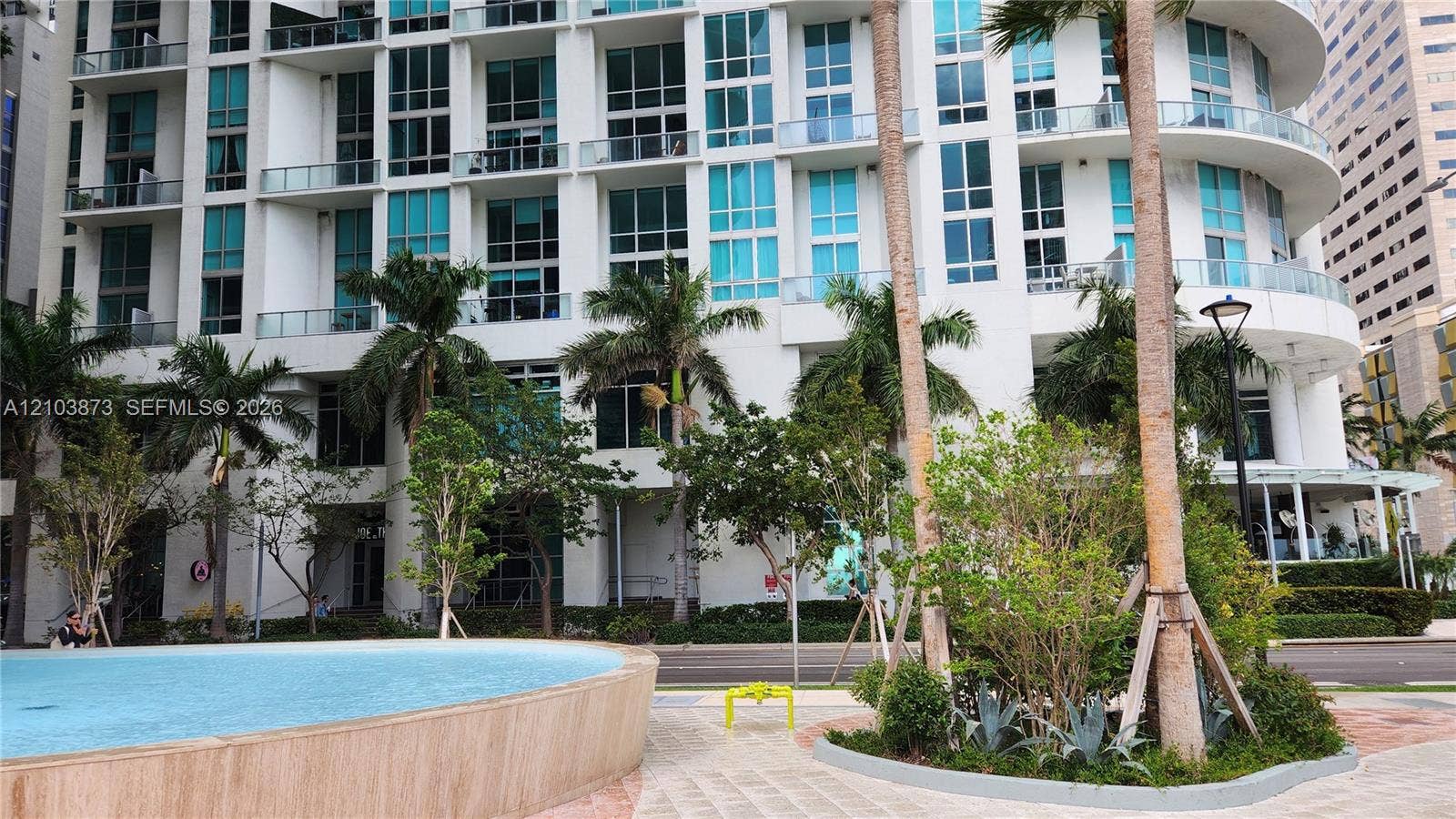 300 S Biscayne Boulevard, #L-808, Miami, FL 33131 High-rise exterior featuring curved architectural design, floor-to-ceiling glass windows, private balconies, a circular water feature, and landscaped grounds with mature palm trees