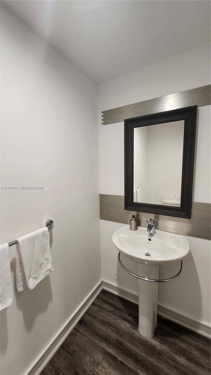 300 S Biscayne Boulevard, #L-808, Miami, FL 33131 Pedestal sink with integrated chrome towel ring, wall-mounted mirror with a dark frame, metallic decorative wall inlay, and wood-finish flooring