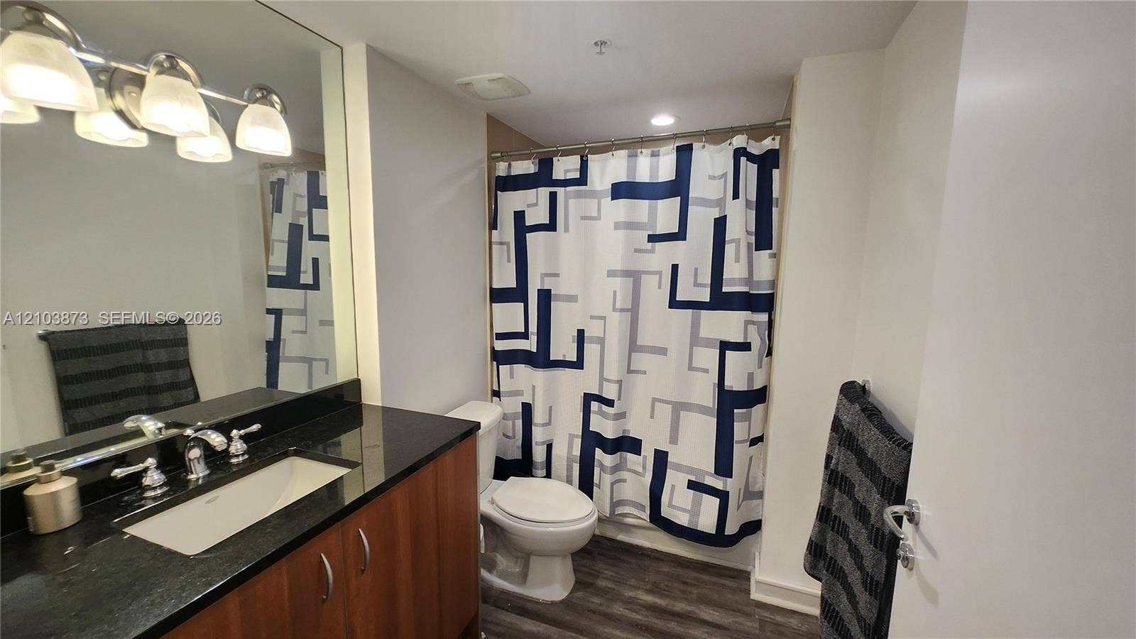 300 S Biscayne Boulevard, #L-808, Miami, FL 33131 Bathroom featuring a dark stone countertop, integrated sink, wood-finish vanity cabinetry, four-light vanity fixture, and full-width wall mirror