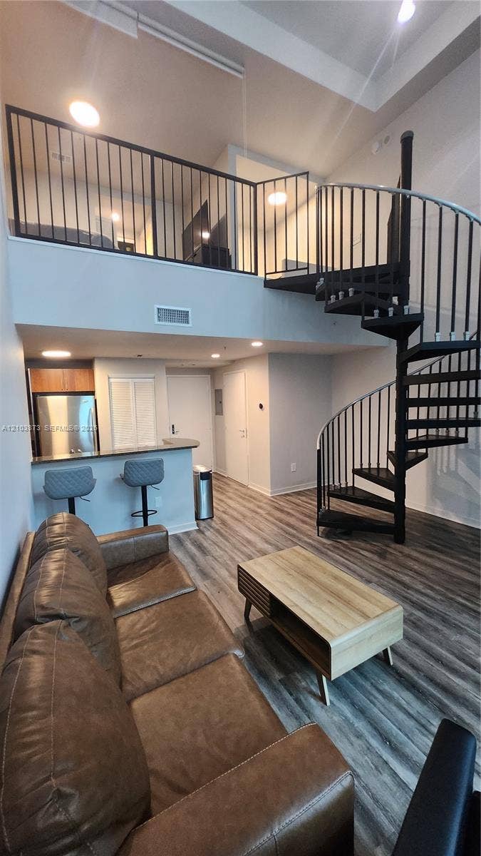 300 S Biscayne Boulevard, #L-808, Miami, FL 33131 High-ceiling living area featuring wood-finish flooring, a metal spiral staircase with matching railing, and a kitchen breakfast bar with integrated stainless steel appliances