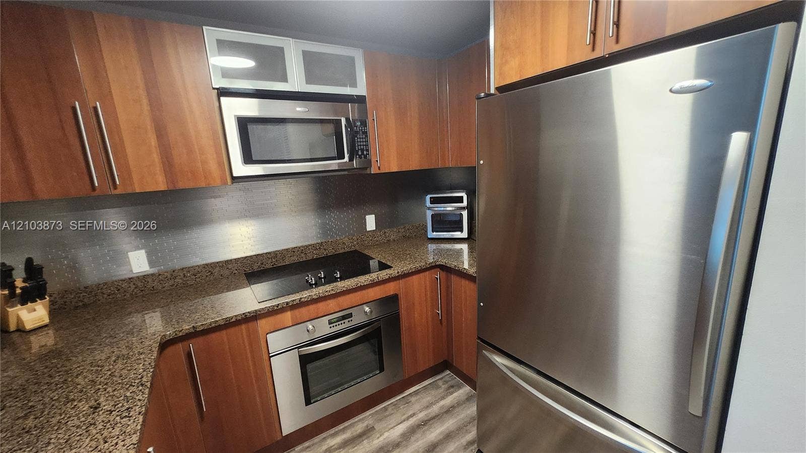 300 S Biscayne Boulevard, #L-808, Miami, FL 33131 Kitchen featuring wood-finish cabinetry, stone countertops, stainless steel appliances, built-in microwave, and wood-finish flooring