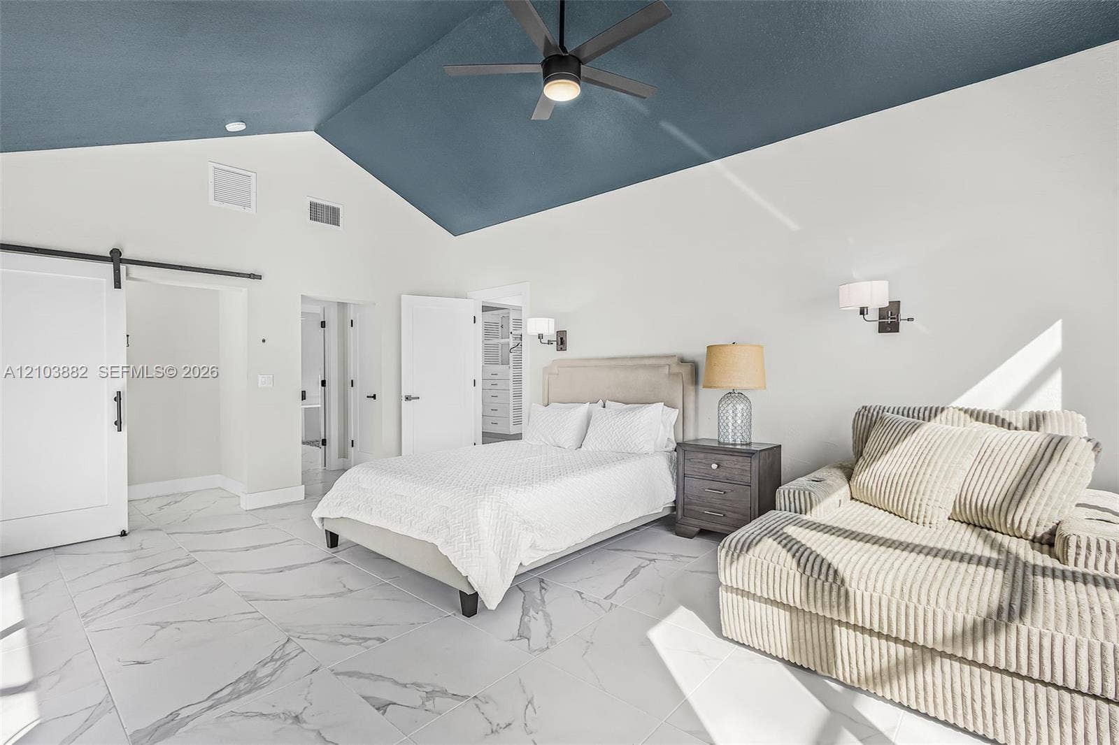 Vaulted ceiling with deep blue accent, large-format stone-finish tile flooring, sliding barn door, and wall-mounted light fixtures