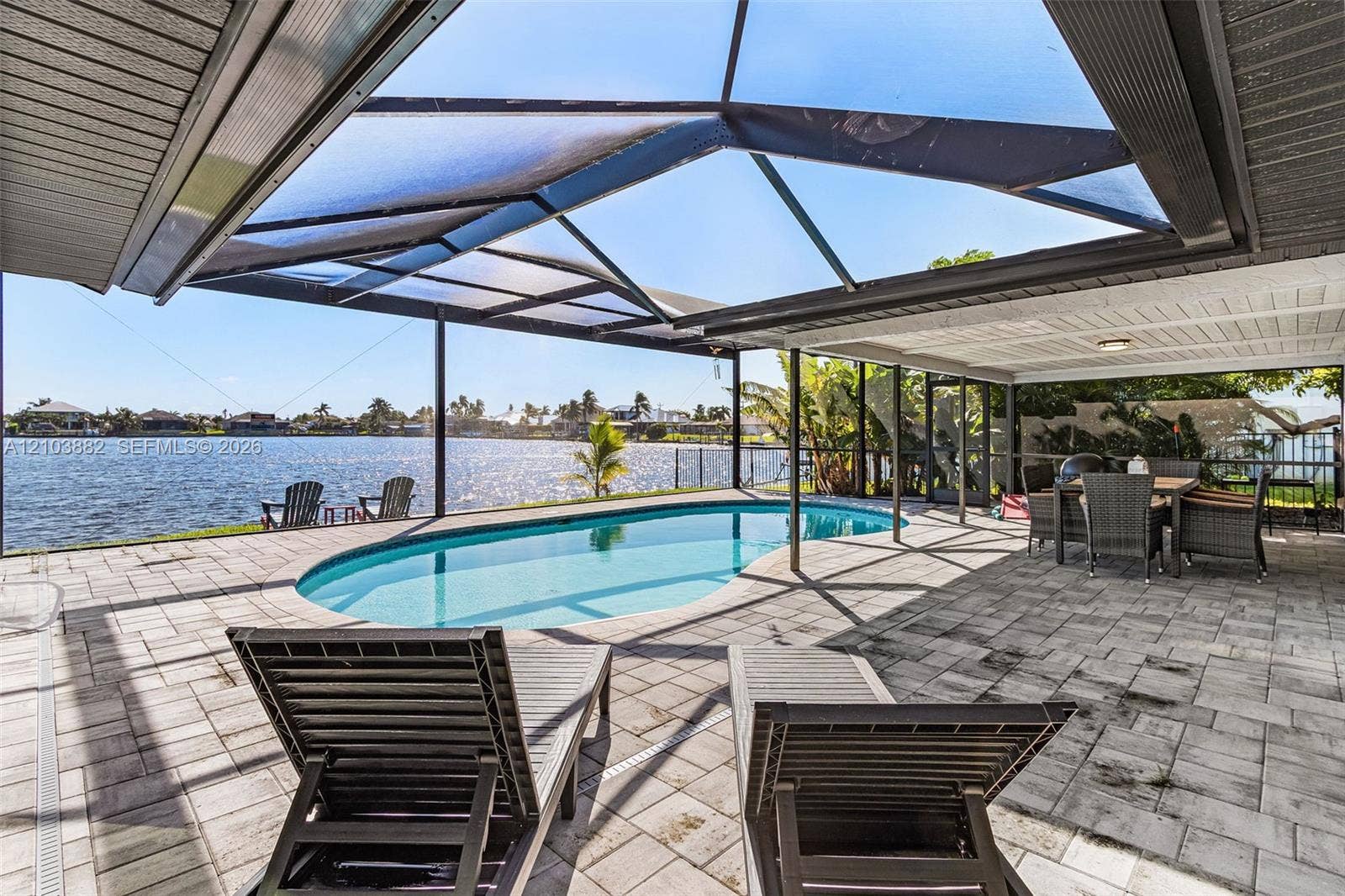 Screen-enclosed patio featuring a paver deck, a kidney-shaped pool, a covered lanai, and waterfront access