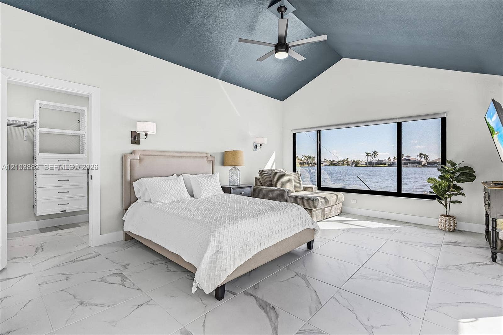 Vaulted ceiling with a matte-finish accent, large-format tile flooring with a stone pattern, floor-to-ceiling panoramic windows, built-in closet organization system, and wall-mounted light fixtures