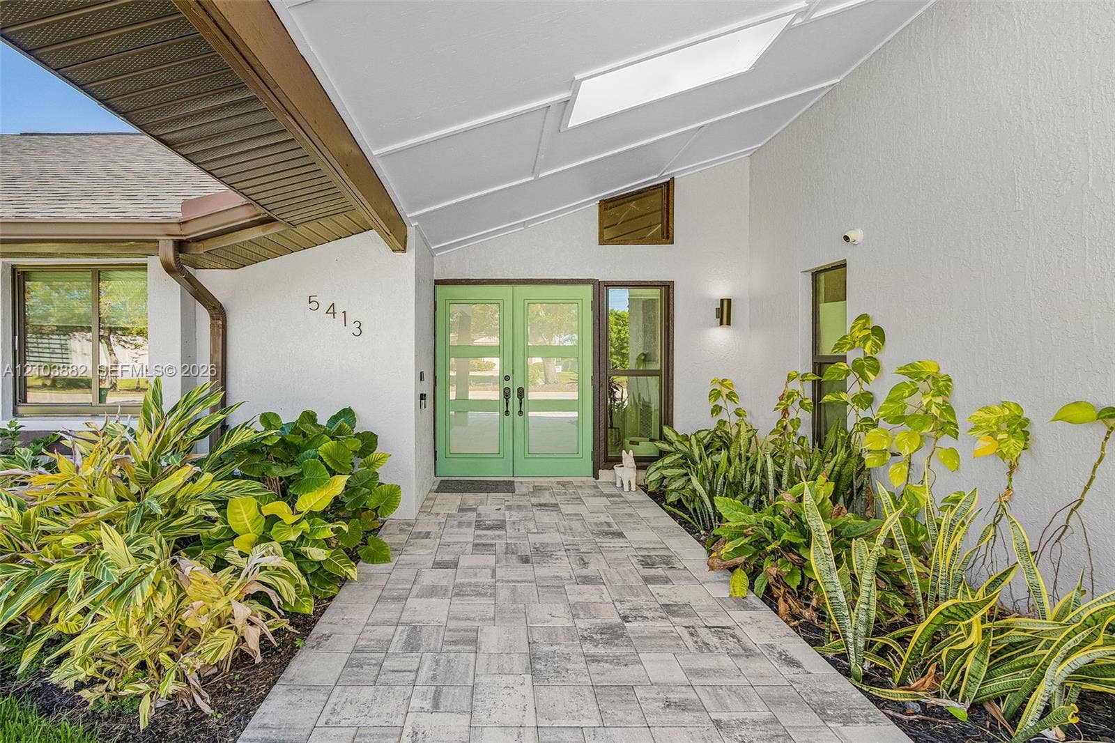 Covered entryway featuring a double-door entry, geometric transom window, stone-finish paver walkway, and exterior wall-mounted lighting