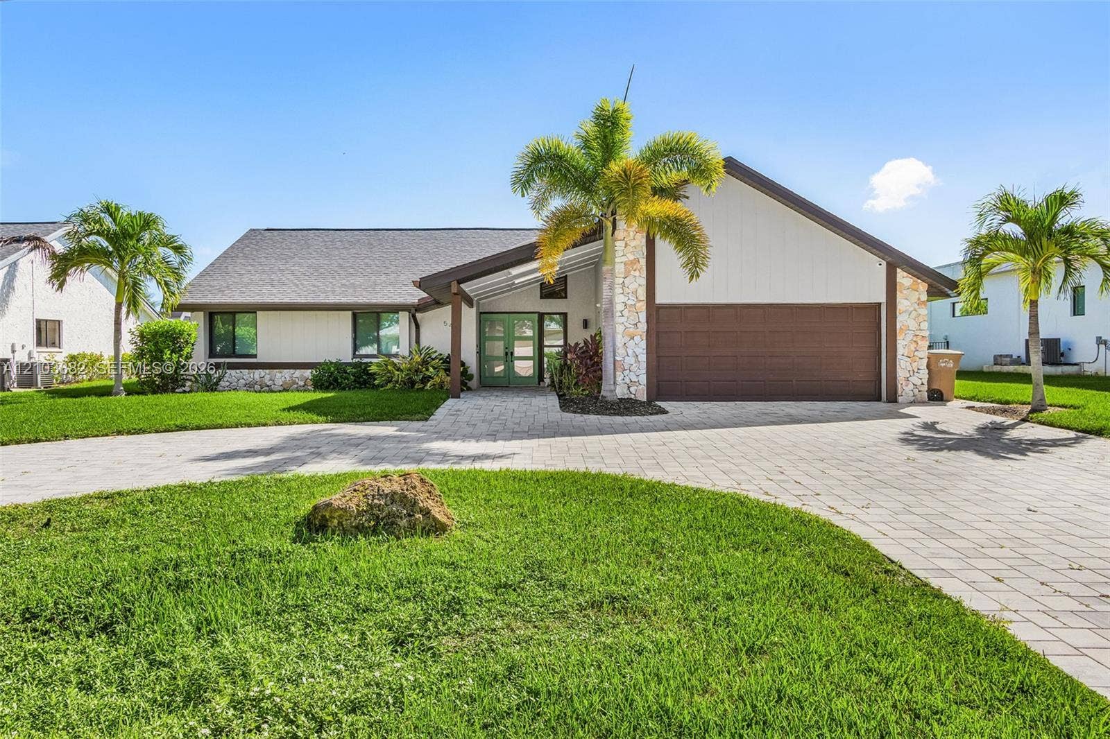 Single-story exterior featuring stone masonry accents, a paved driveway, double-entry doors, and a multi-car garage