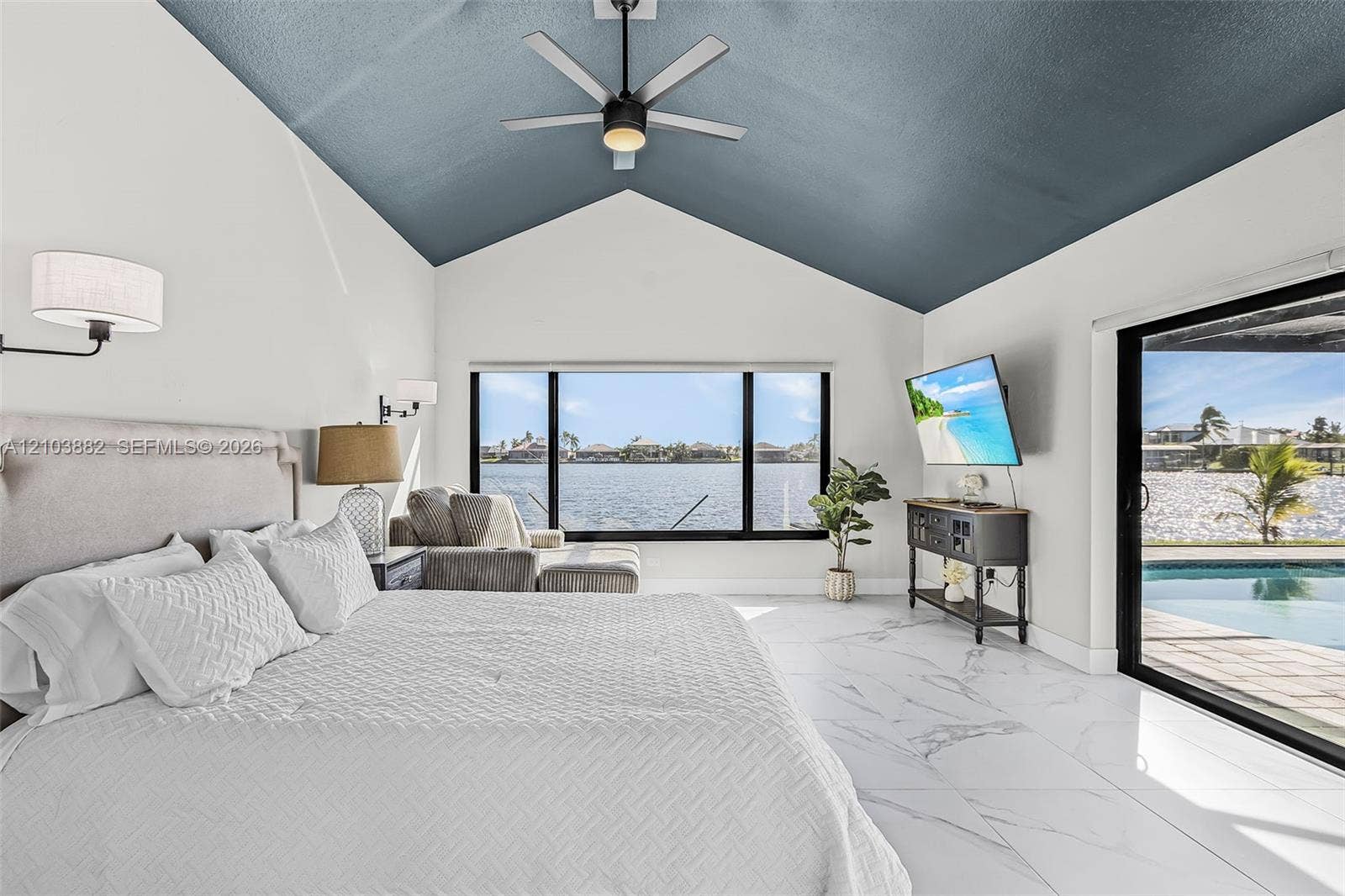 Vaulted ceiling with accented blue finish, large-format tile flooring with marble-style veining, ceiling fan with integrated lighting, oversized picture window, and sliding glass door access to the pool area
