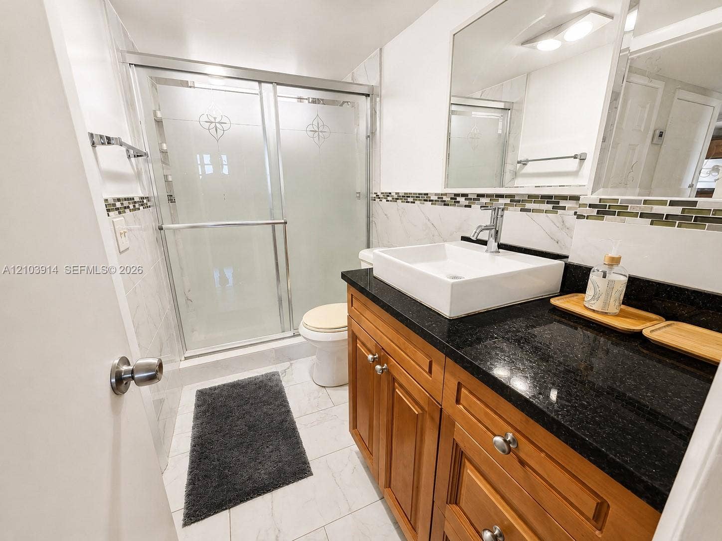 Bathroom featuring a natural wood vanity with a black countertop, rectangular vessel sink, polished chrome faucet, and a walk-in shower with etched glass sliding doors
