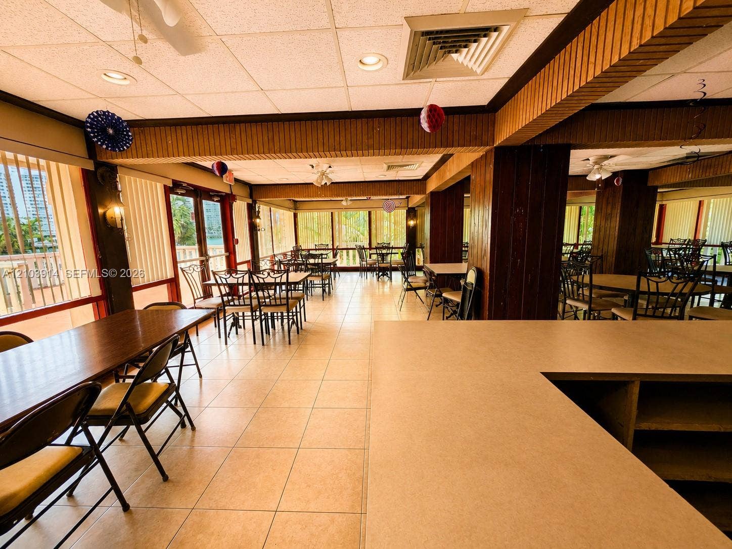 Large open floor plan featuring tile flooring, exposed structural pillars with wood-finish detailing, recessed lighting, and expansive windows