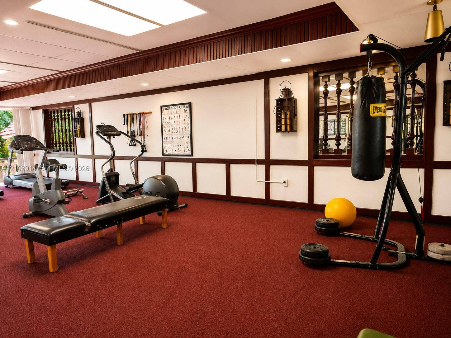 Spacious room featuring dark wood wainscoting with decorative trim, recessed ceiling lighting, a dedicated inset mirrored wall, and wall-mounted light fixtures