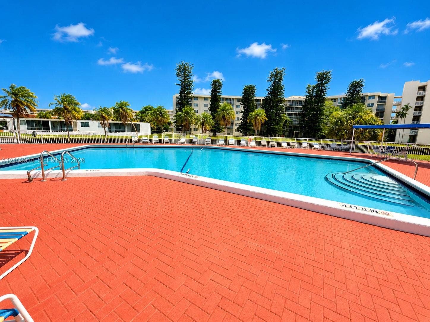 Swimming pool featuring a herringbone-patterned paved deck, integrated stairs for entry, stainless steel handrails, and surrounding perimeter fencing