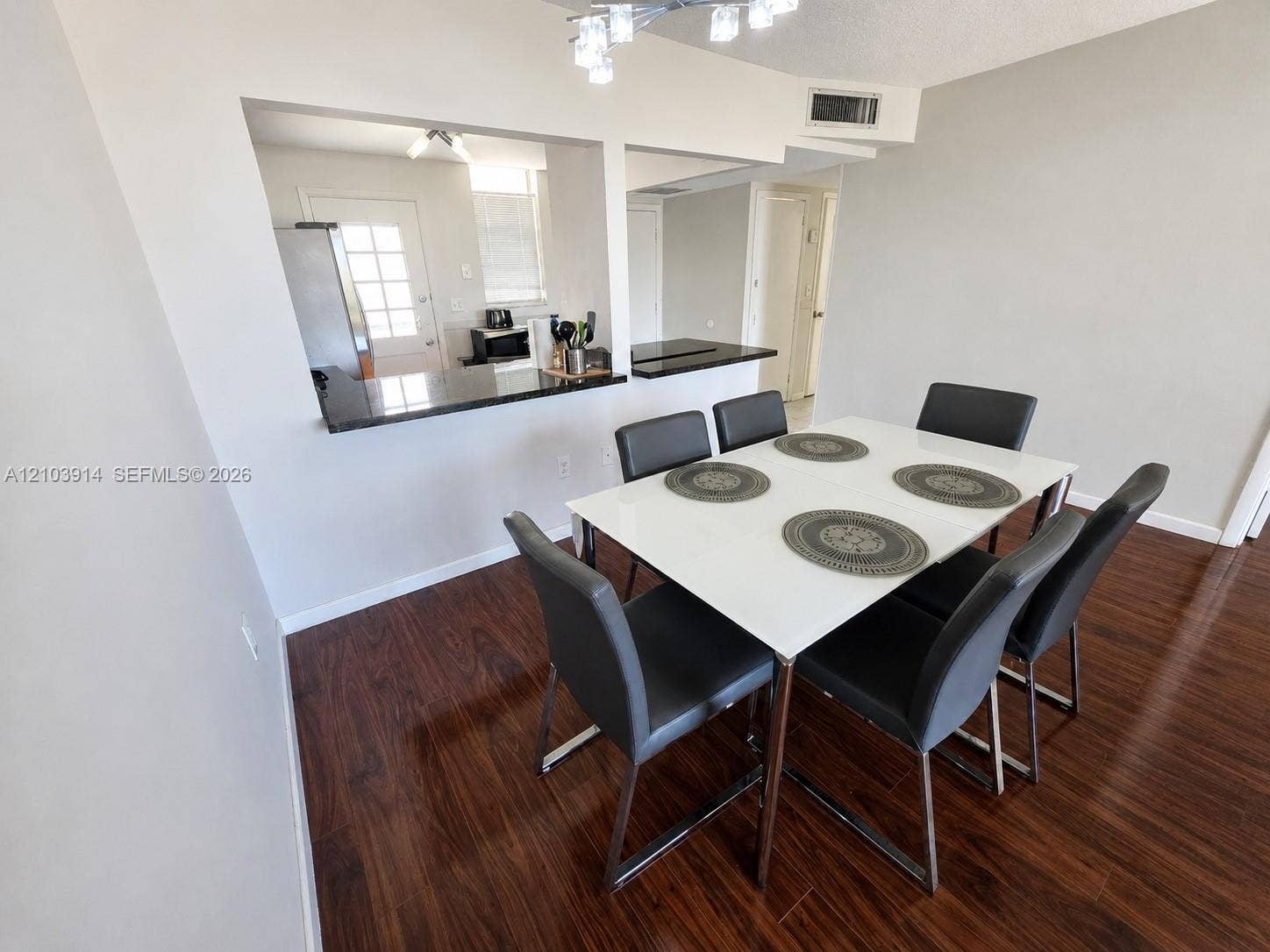 Dining area featuring wood-finish flooring, a pass-through opening, dark stone-surface breakfast bar, and multi-light ceiling fixture