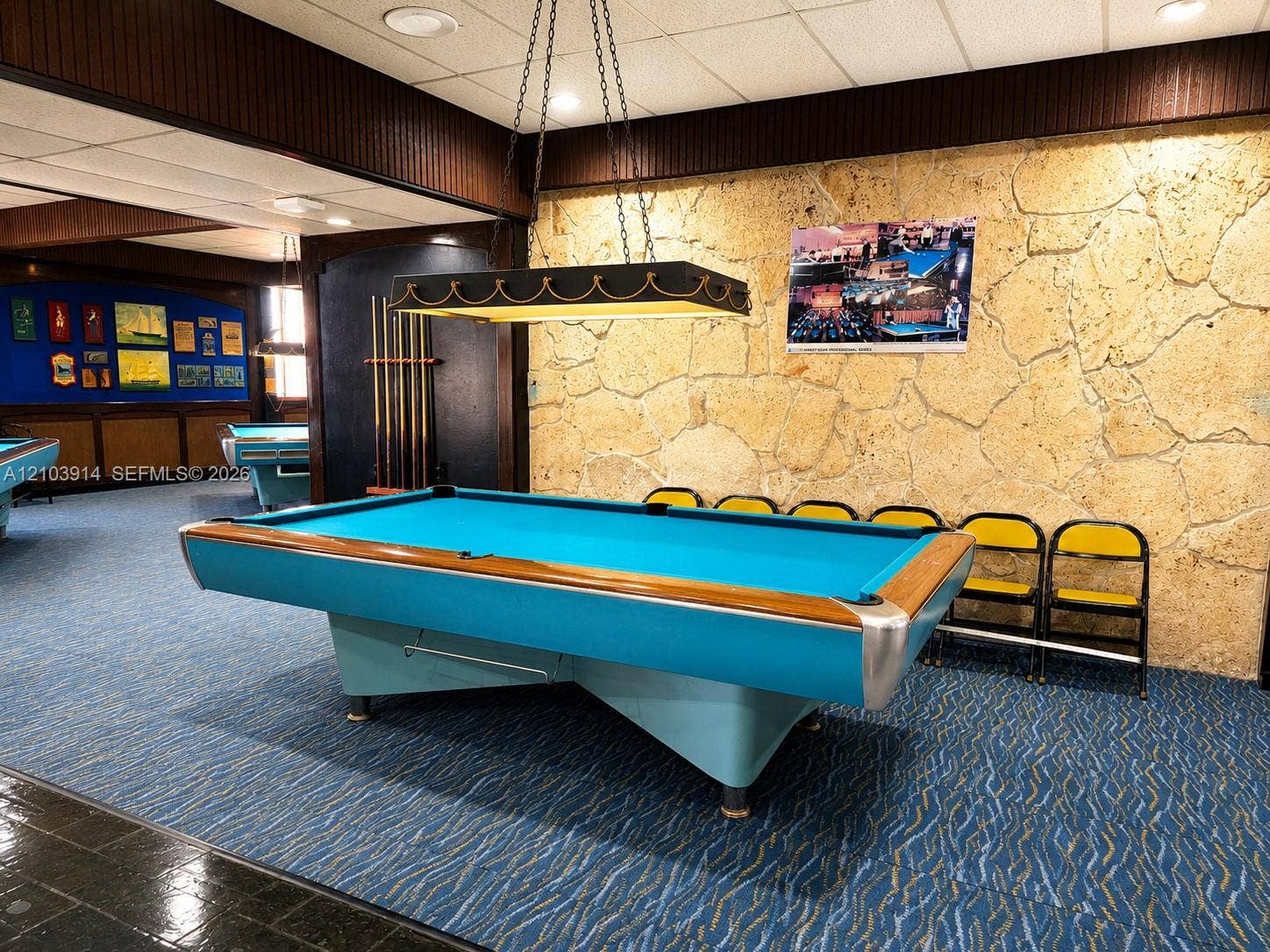 Textured stone accent wall, decorative hanging billiard light fixture, dark wood-paneling trim, and built-in wall-mounted pool cue rack