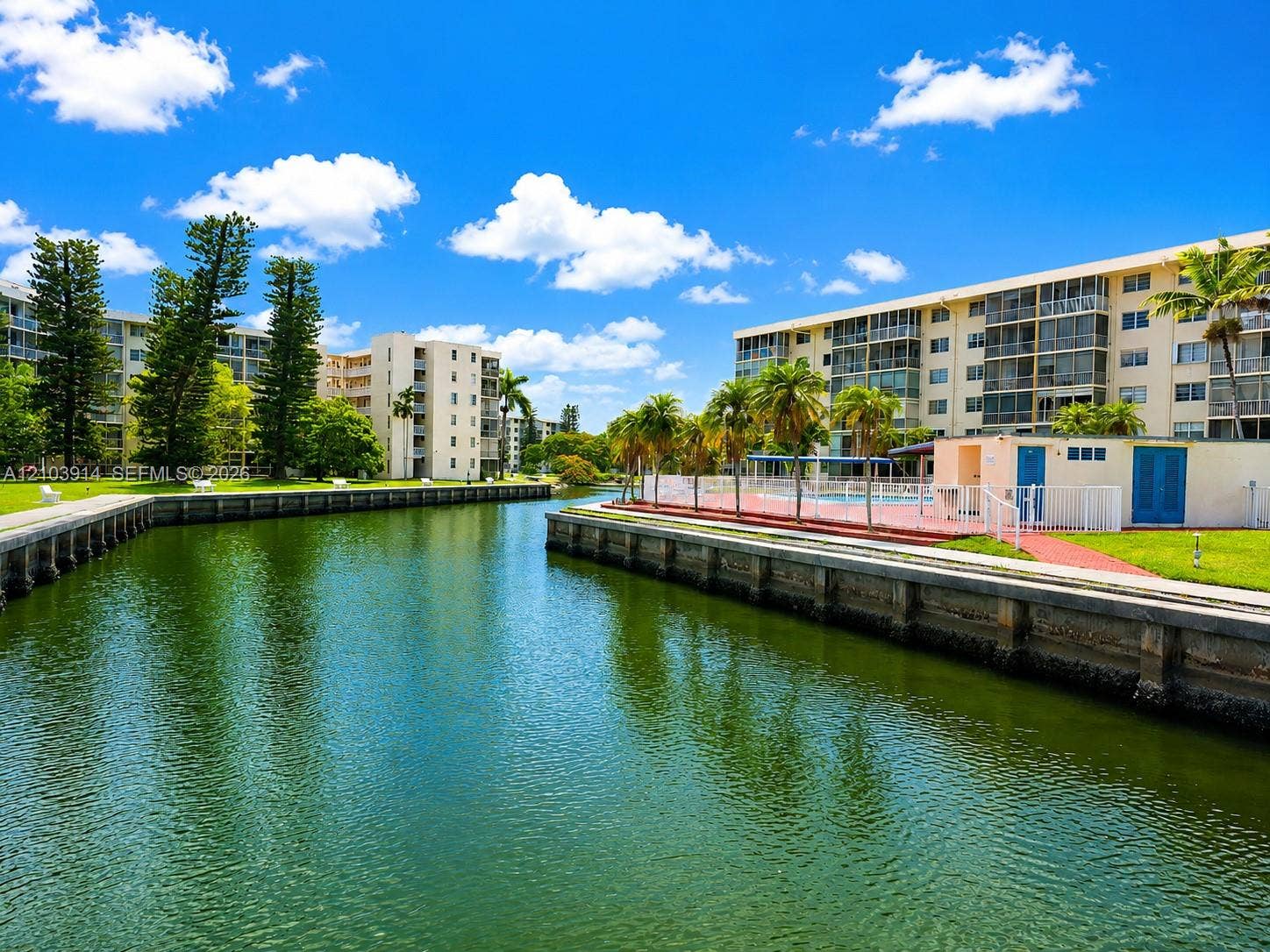 Waterfront exterior featuring a concrete bulkhead, swimming pool, manicured lawn, and mature palm trees