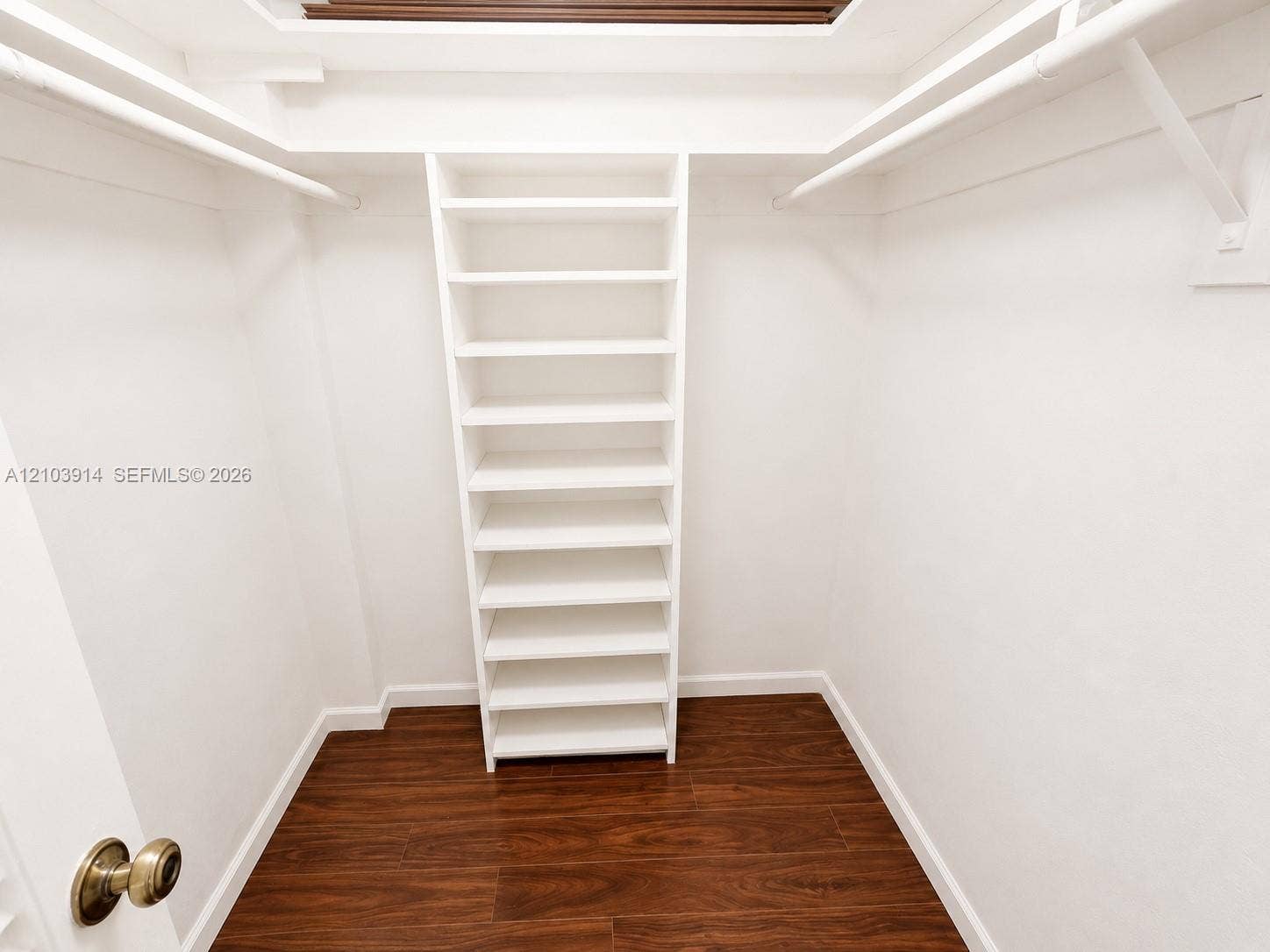 Walk-in closet featuring white built-in shelving, dual tiered hanging rods, and wood-finish flooring