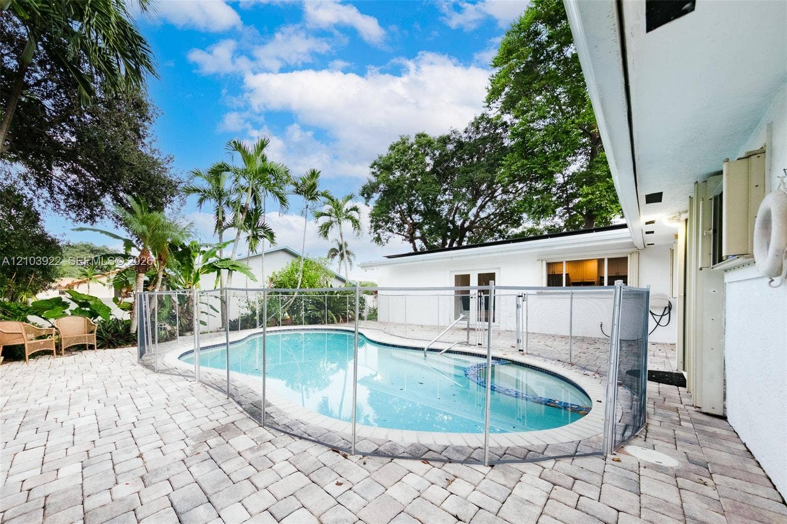 Resort-style pool with safety fencing, surrounded by paver patio, with exterior lighting and lush landscaping