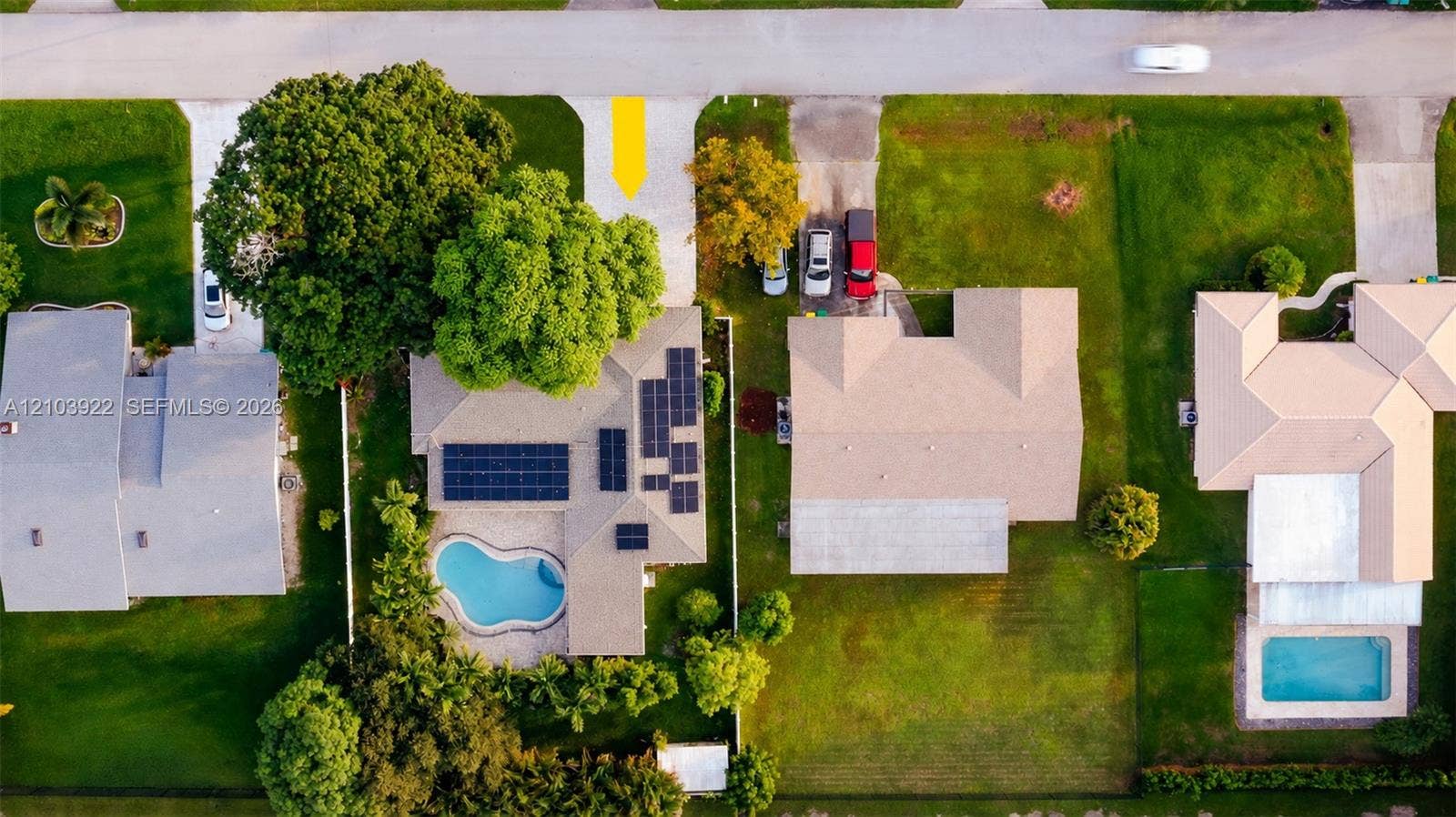Private swimming pool with surrounding patio, solar panels on the roof, and lush mature trees