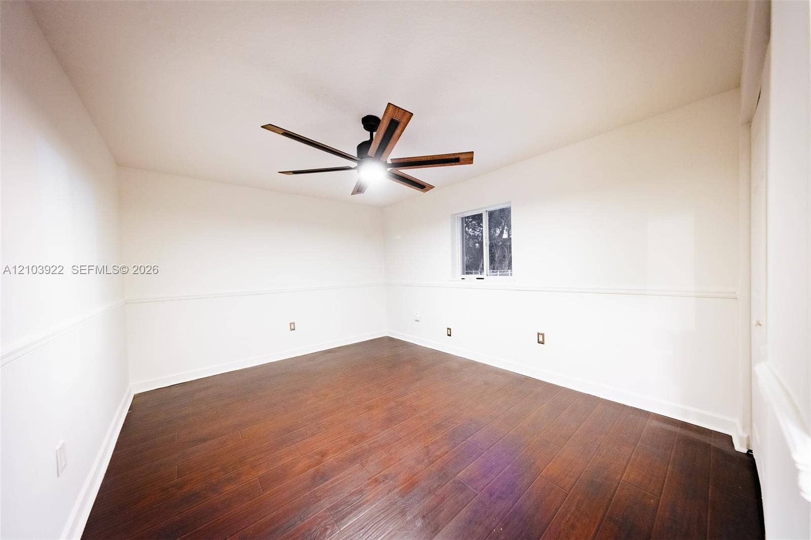 Wood-finish flooring, white walls with wainscoting, and a modern ceiling fan with integrated lighting