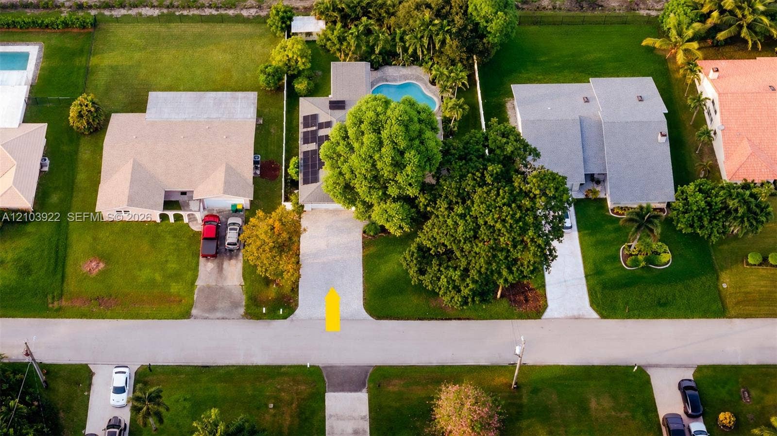 Manicured lawn, mature trees, concrete driveway, paved road, and a neighboring swimming pool