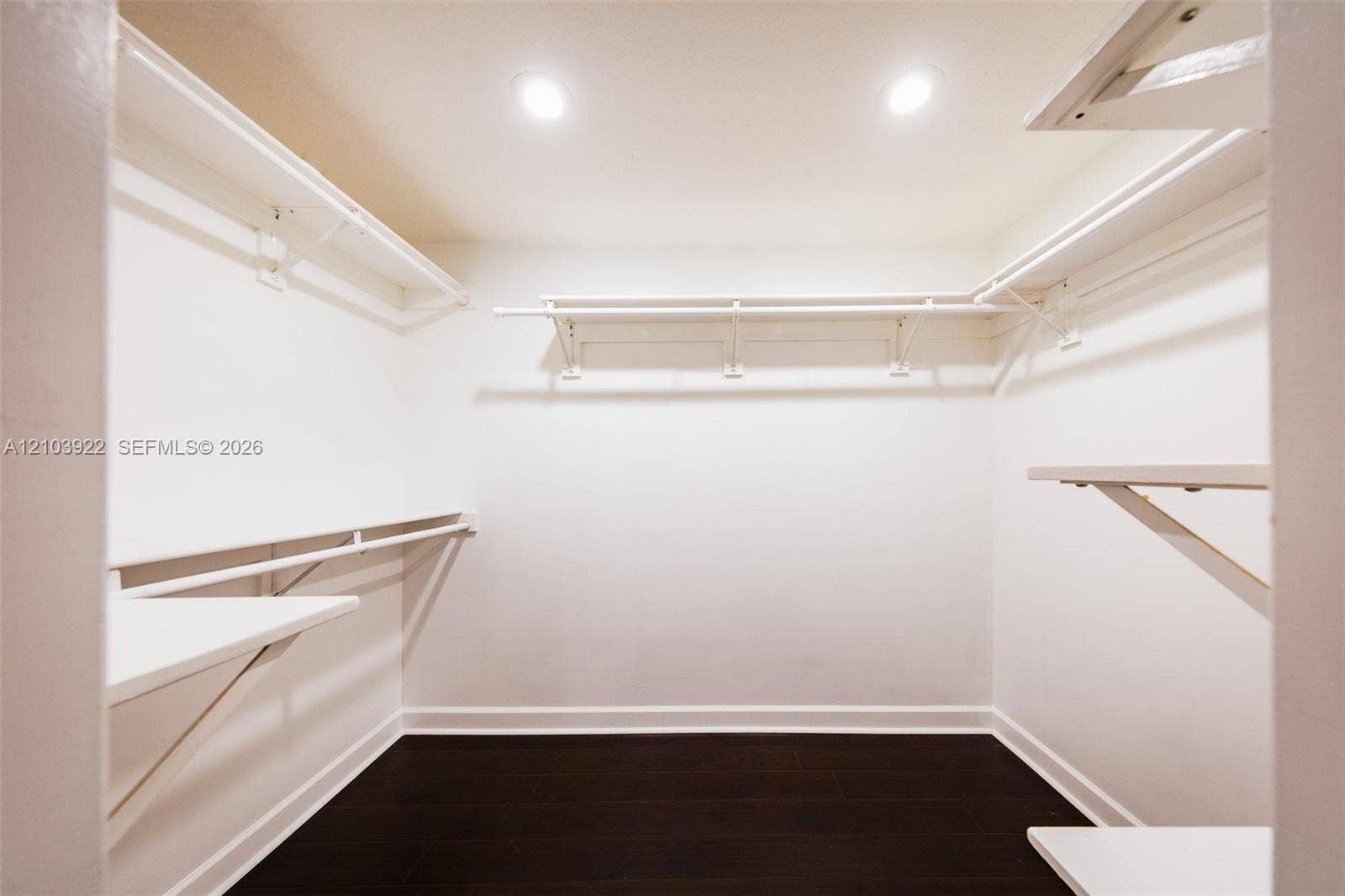 Recessed lighting illuminates the dark wood-finish flooring and white walls