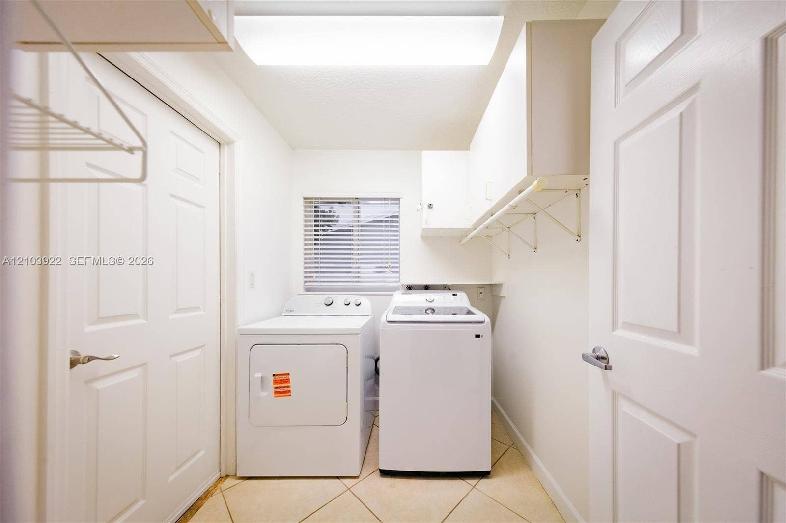 Laundry area with tile flooring, window with blinds, and white cabinetry
