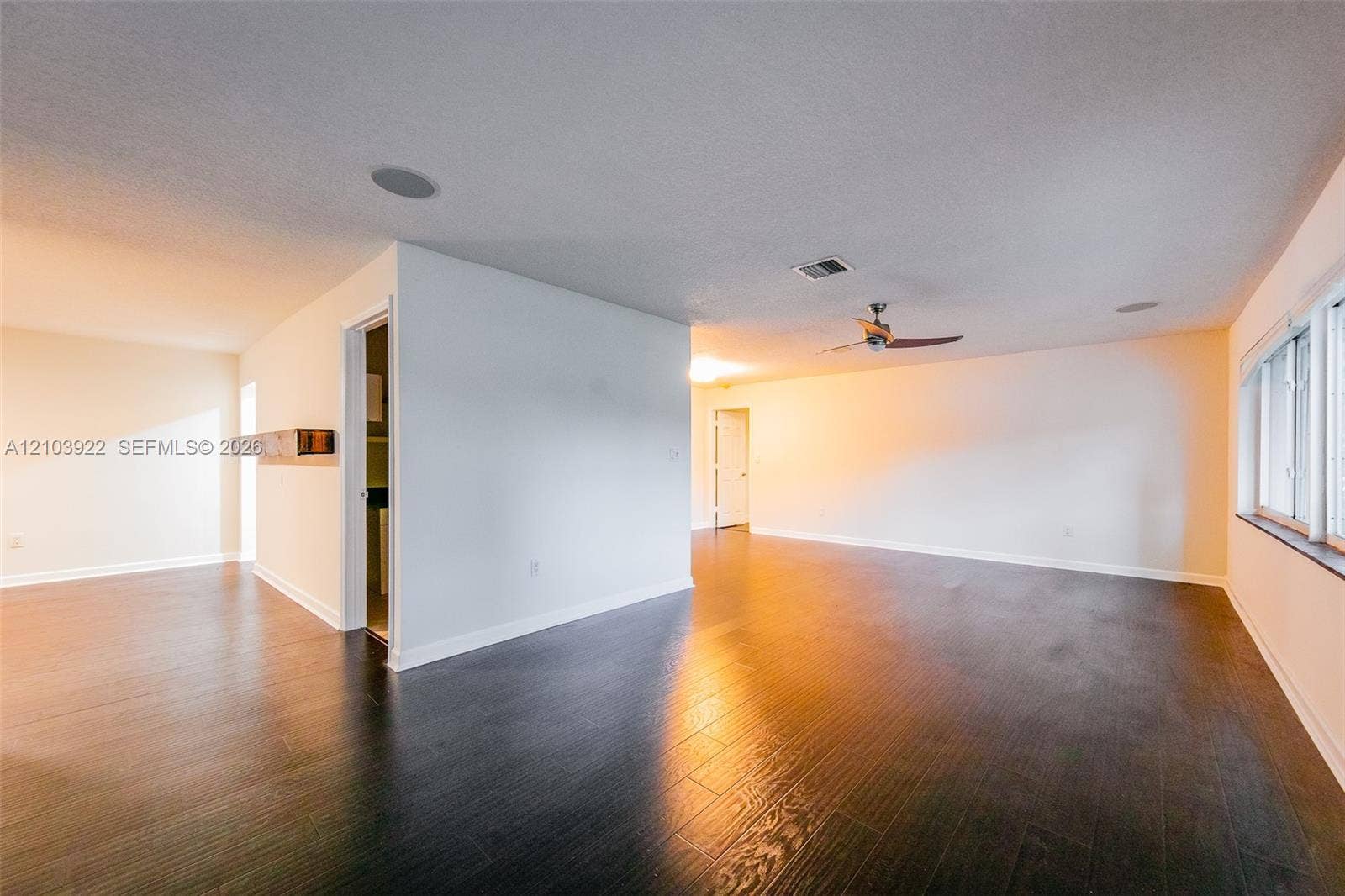 Expansive room featuring dark wood-finish flooring, white walls, multiple windows, recessed lighting, and a ceiling fan