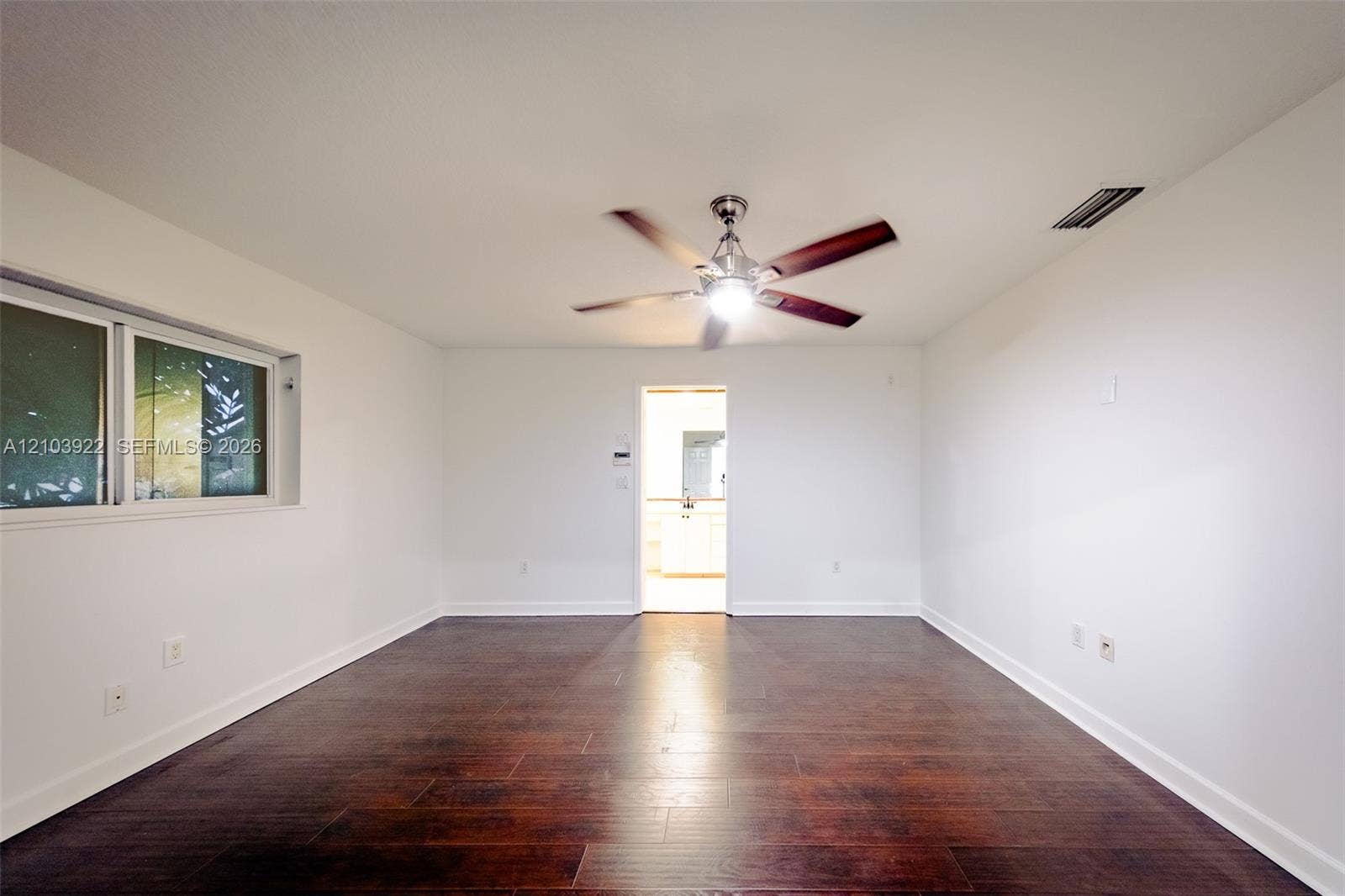 Dark wood-finish flooring with white baseboards, a ceiling fan with integrated lighting, and a window with white framing